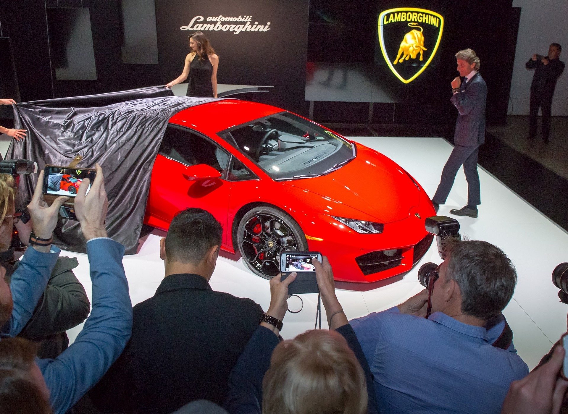 Red Lamborghini Huracán LP580-2 being unveiled at a press event with attendees photographing the car