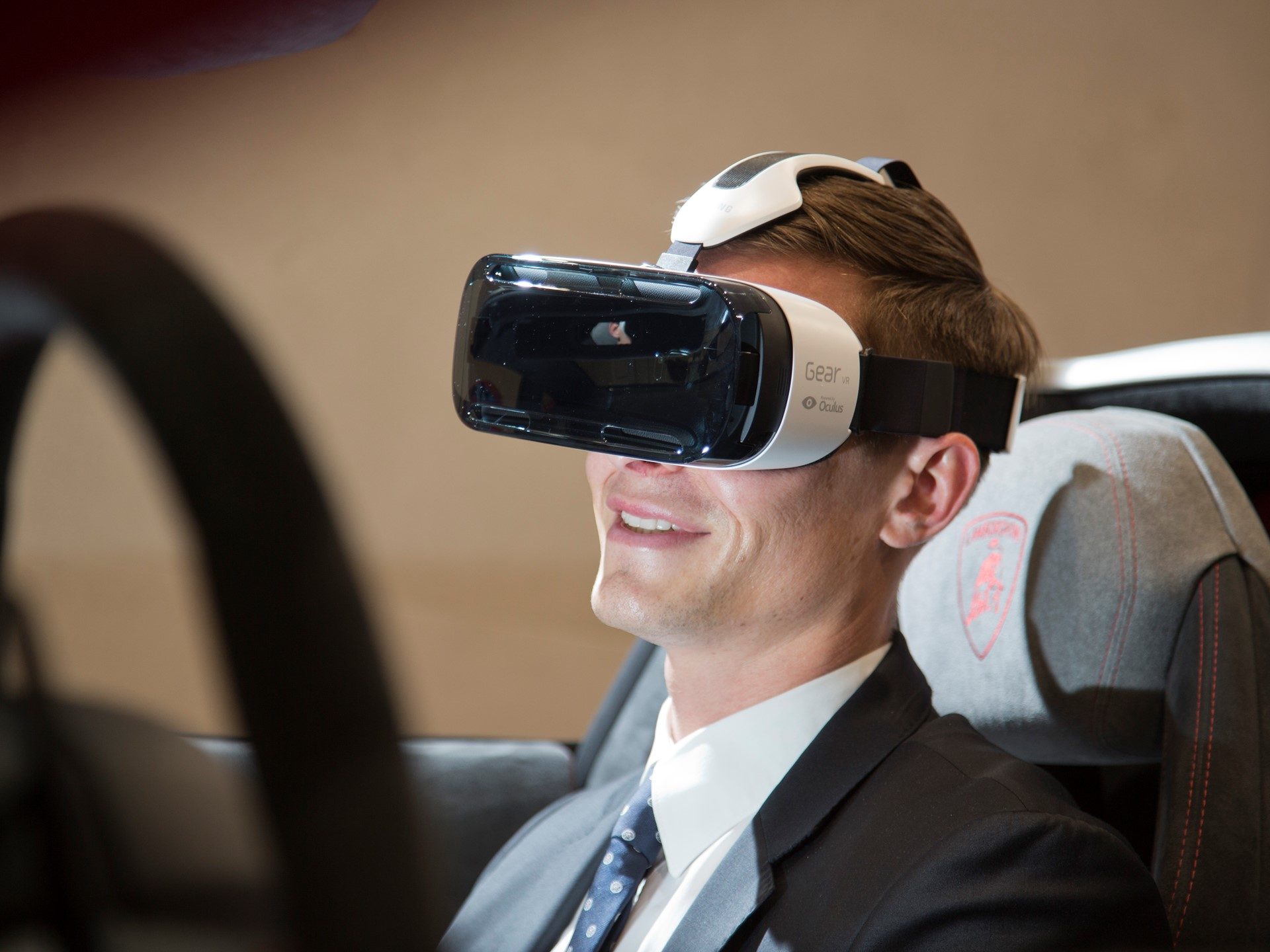 Participant wearing Samsung Gear VR headset in a Lamborghini Huracán cockpit with the steering wheel and red-embroidered Lamborghini seat logo visible