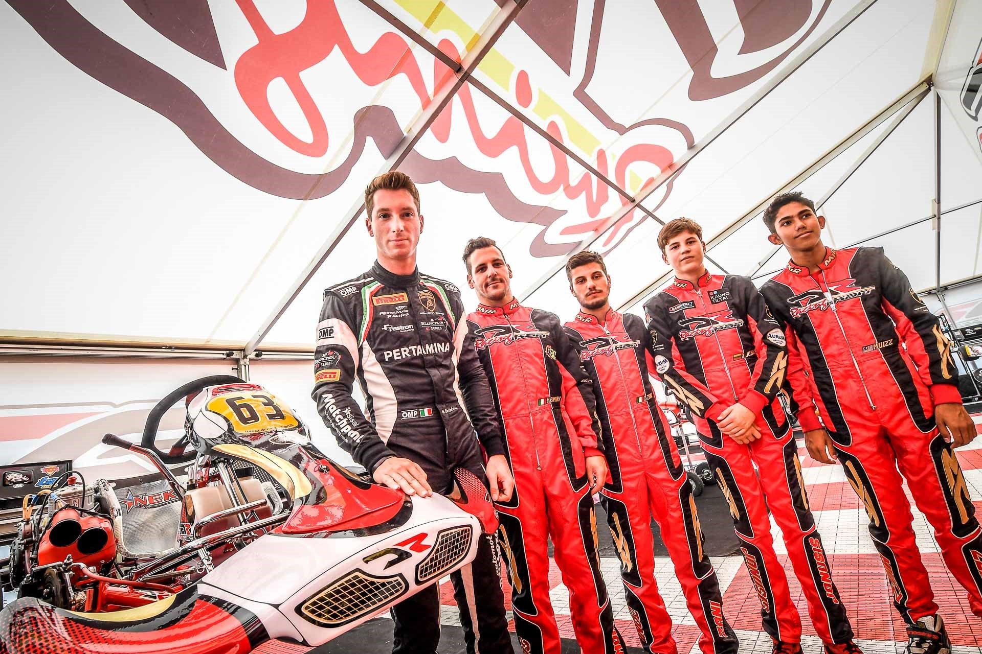 Kart Drivers Program participants in red and black racing suits standing with a DR Racing Kart under a branded tent at Adria