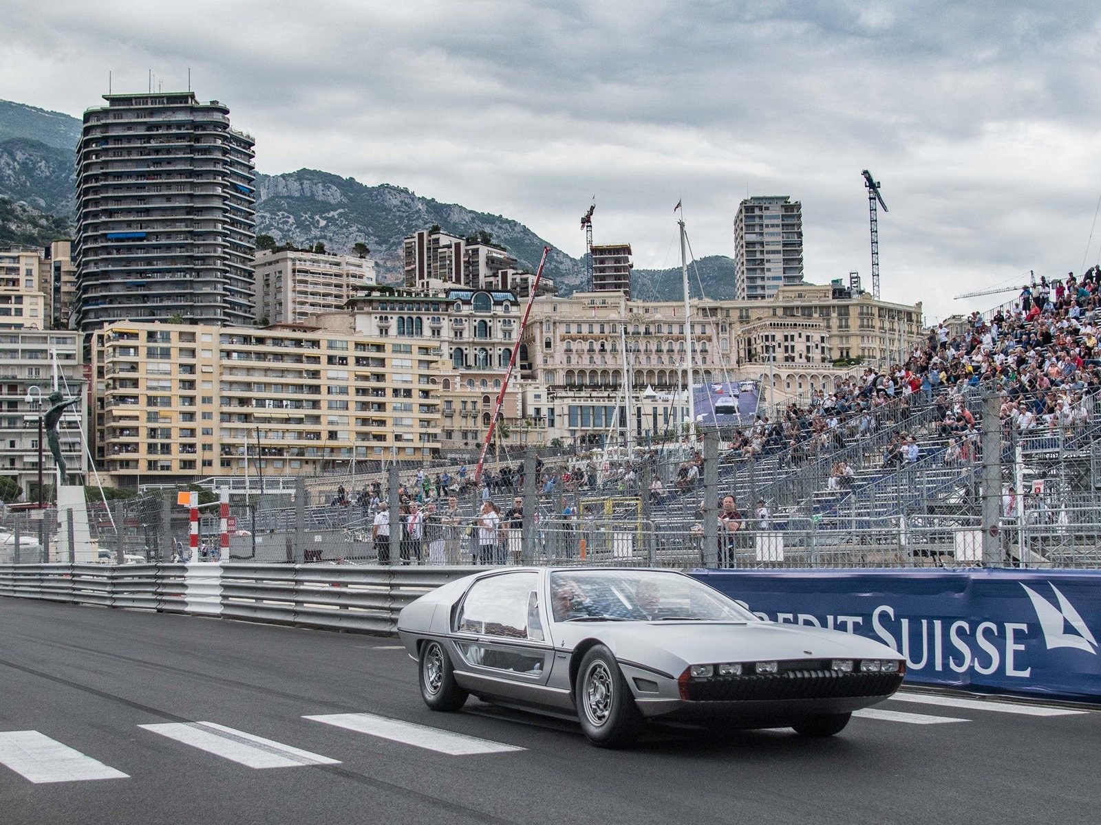 Lamborghini Marzal concept car in silver driving on the Monaco circuit under cloudy skies with spectators visible in grandstands
