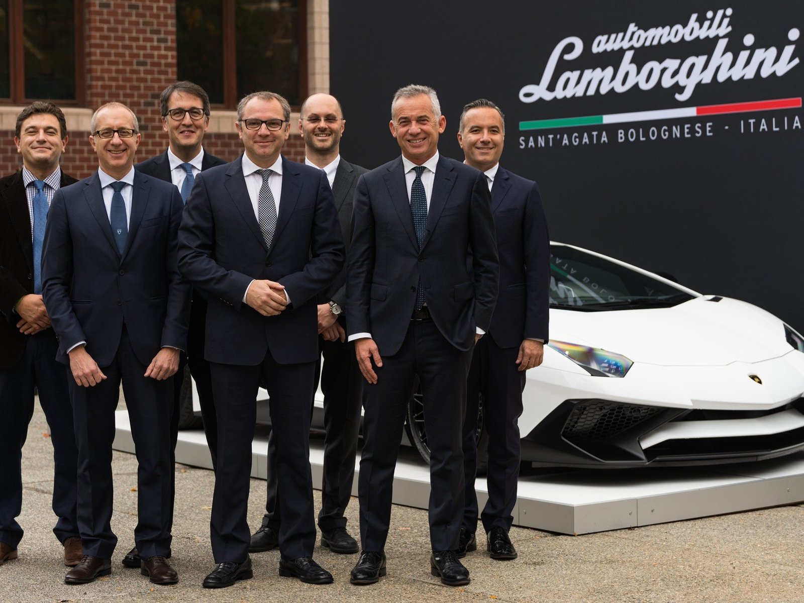 Executives from Automobili Lamborghini and the MIT-Italy Program stand before a white Lamborghini Aventador during the formal partnership signing event