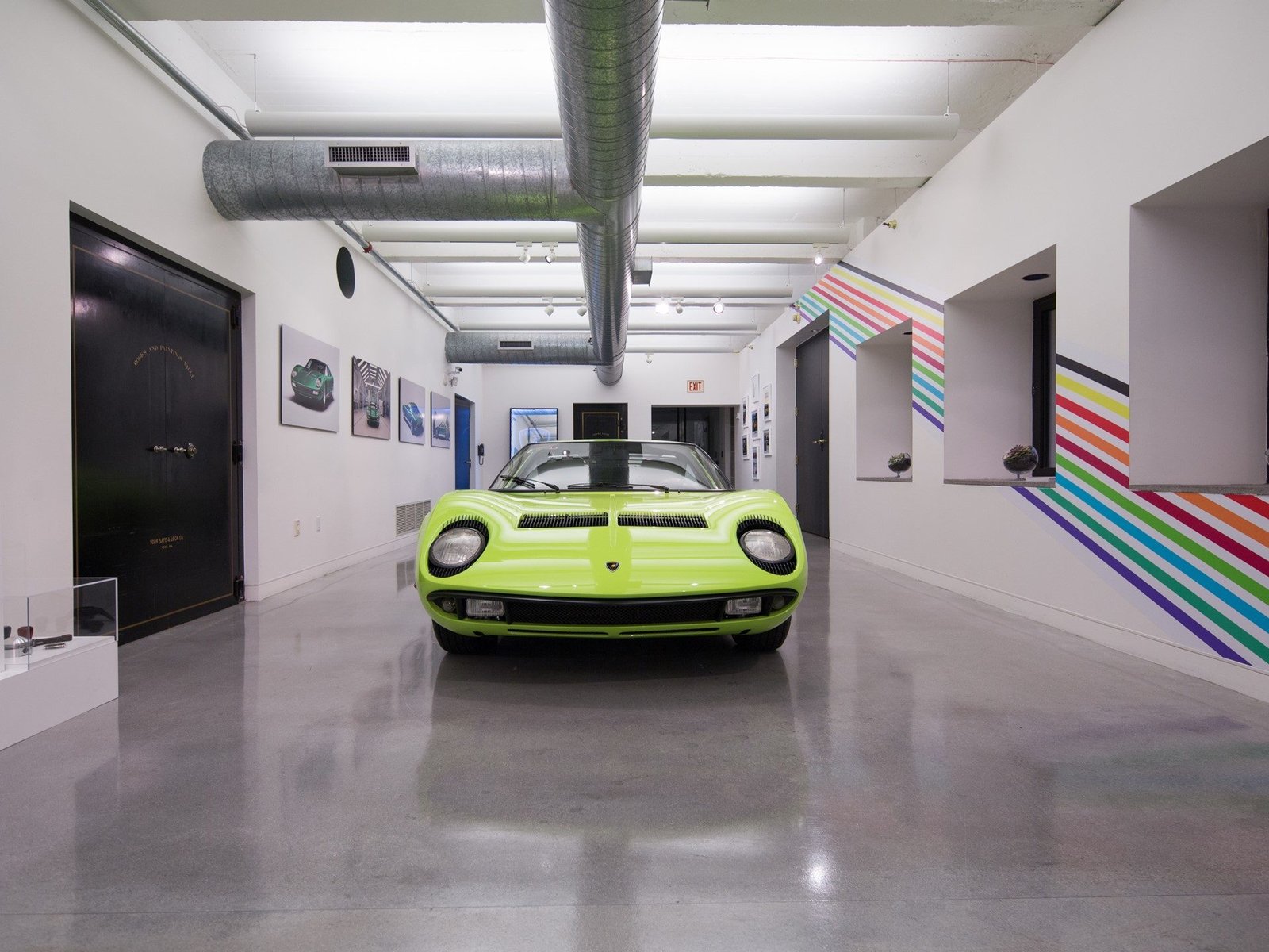 A vibrant lime green 1968 Lamborghini Miura displayed in a minimalist gallery at The Wolfsonian-FIU during Art Basel Miami Beach, with framed archival photographs on the walls behind it.
