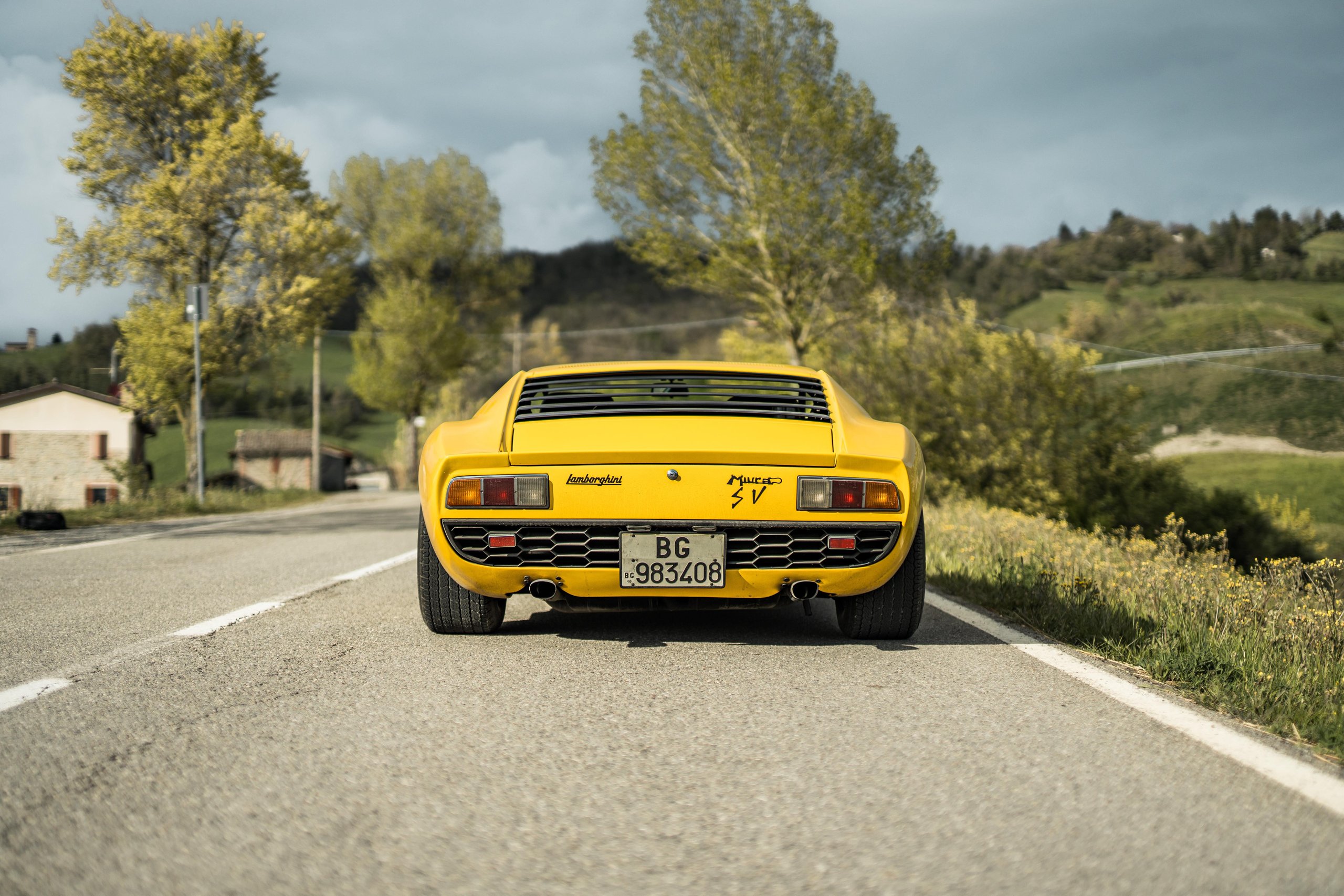 Rear view of a yellow lamborghini miura sv showing wide fenders, rear louvers, and honeycomb grilles