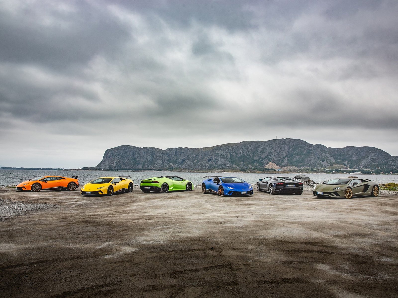Lamborghini Huracán and Aventador convoy on a dirt road beside a Norwegian fjord with mountains in the background