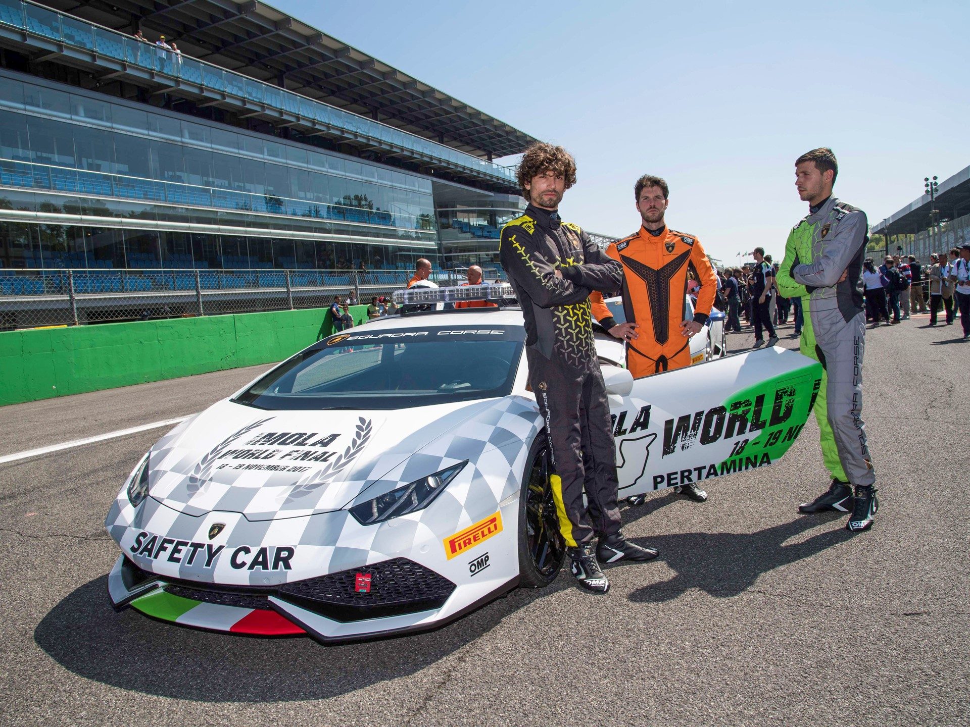 Three drivers in racing suits standing beside a Lamborghini Huracan safety car at a professional racetrack event