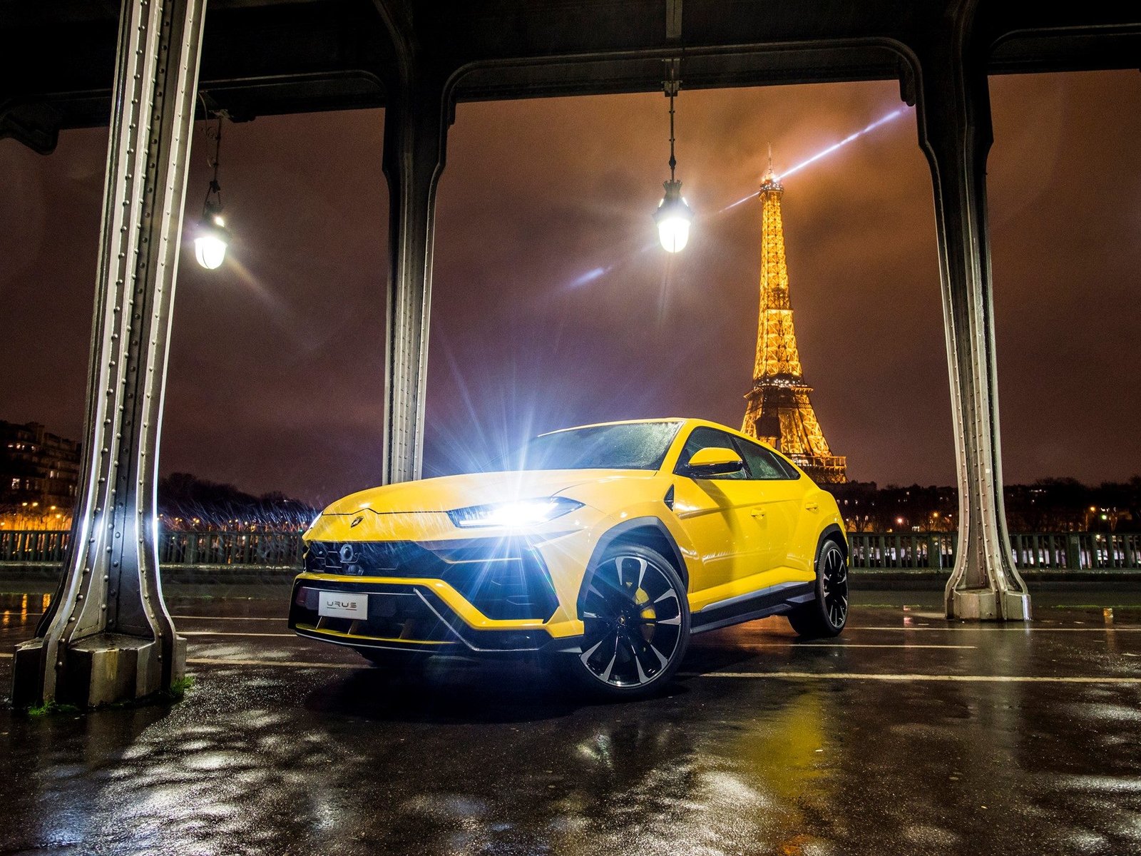 Yellow Lamborghini Urus parked on a wet Paris street at night with the illuminated Eiffel Tower in the background