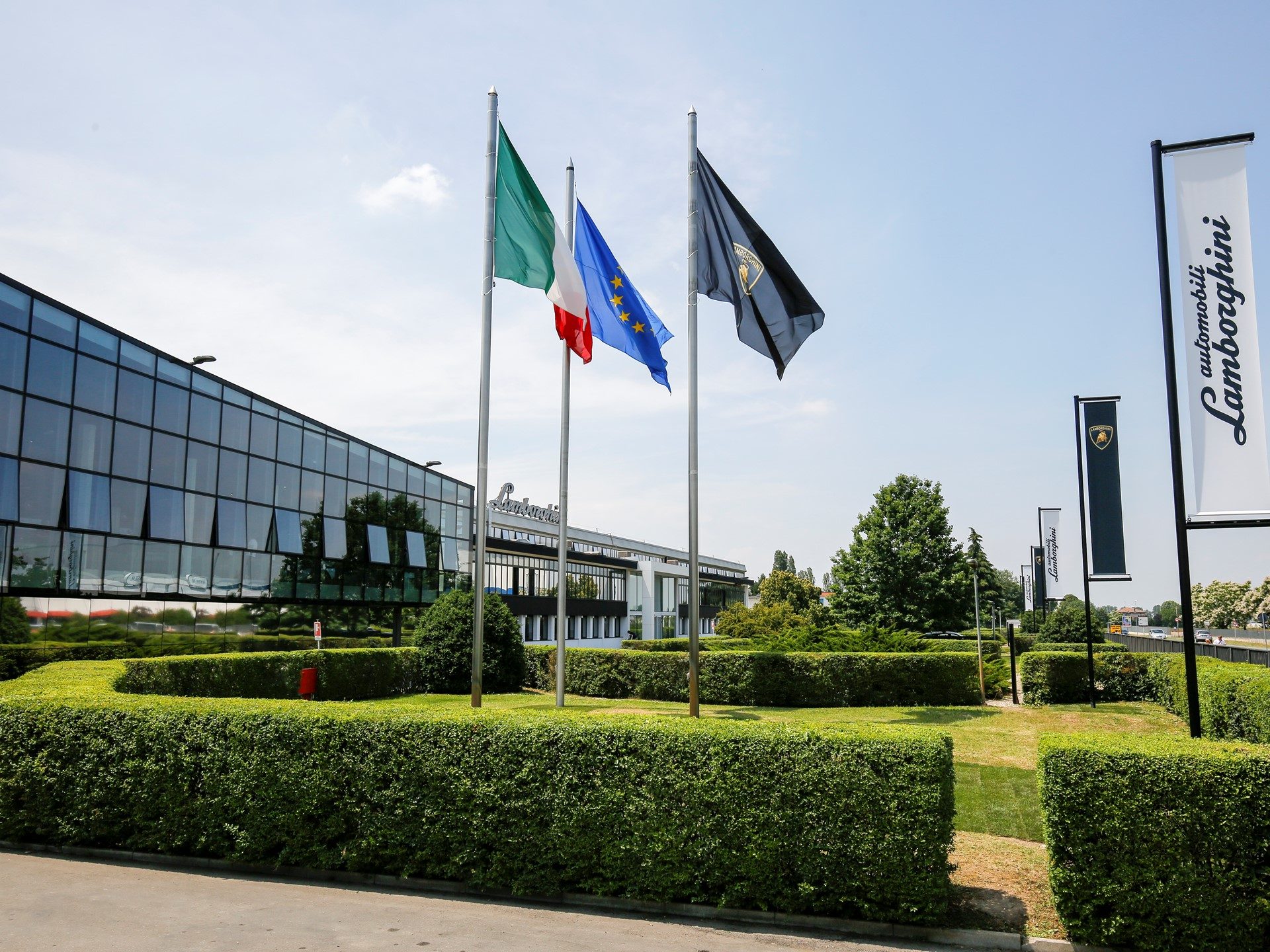 Lamborghini factory headquarters in Sant'Agata Bolognese with Italian, EU, and Lamborghini flags flying under clear skies