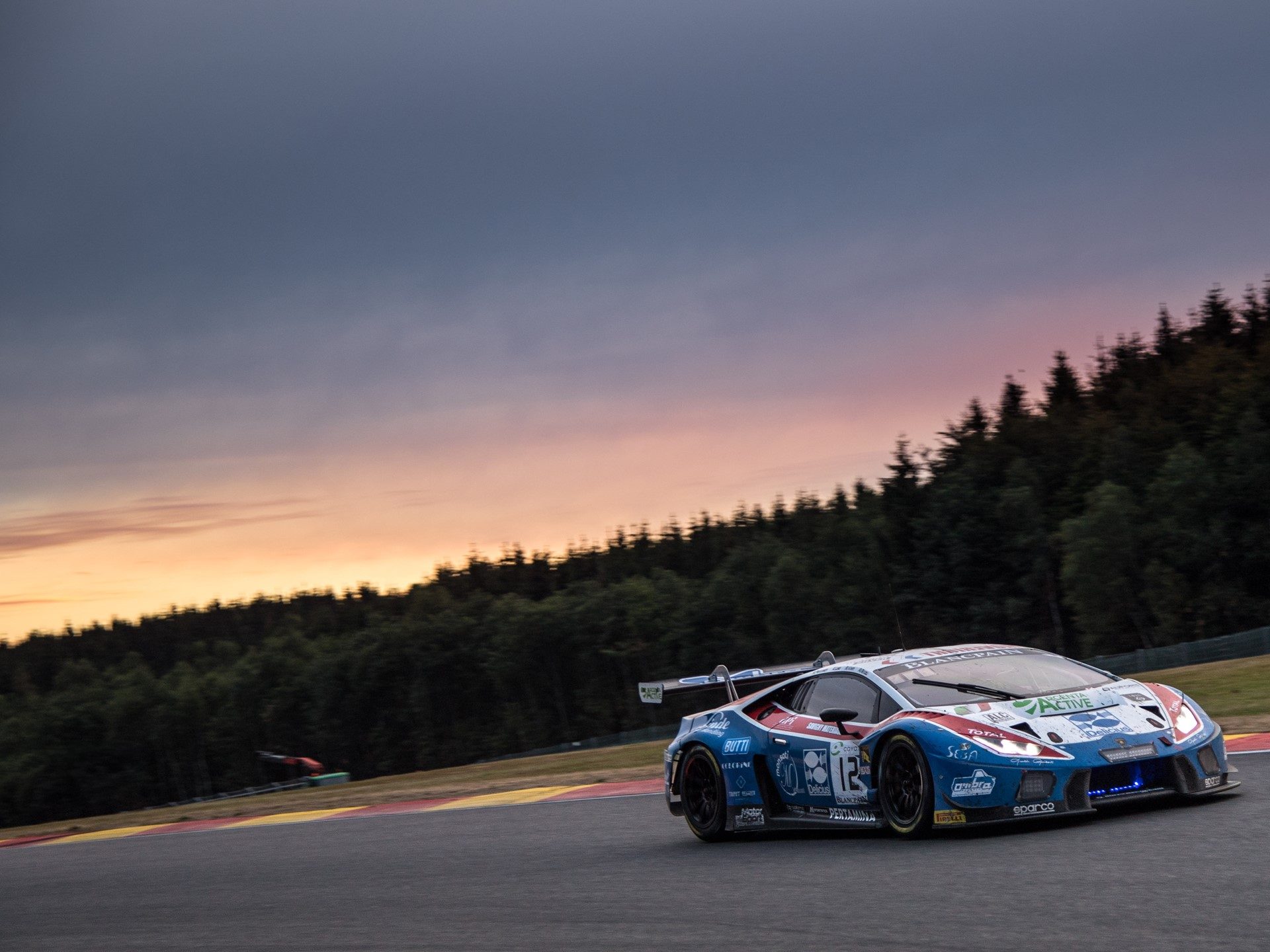 Lamborghini Huracán GT3 racing at Spa-Francorchamps during the 2018 24 Hours with a vivid sunset sky behind the circuit