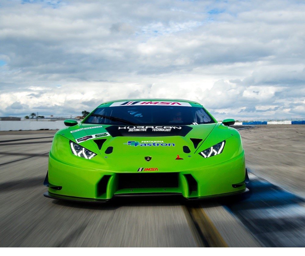 A green Lamborghini Huracán GT3 race car at speed on a racetrack, showcasing its aggressive front aerodynamics and racing livery