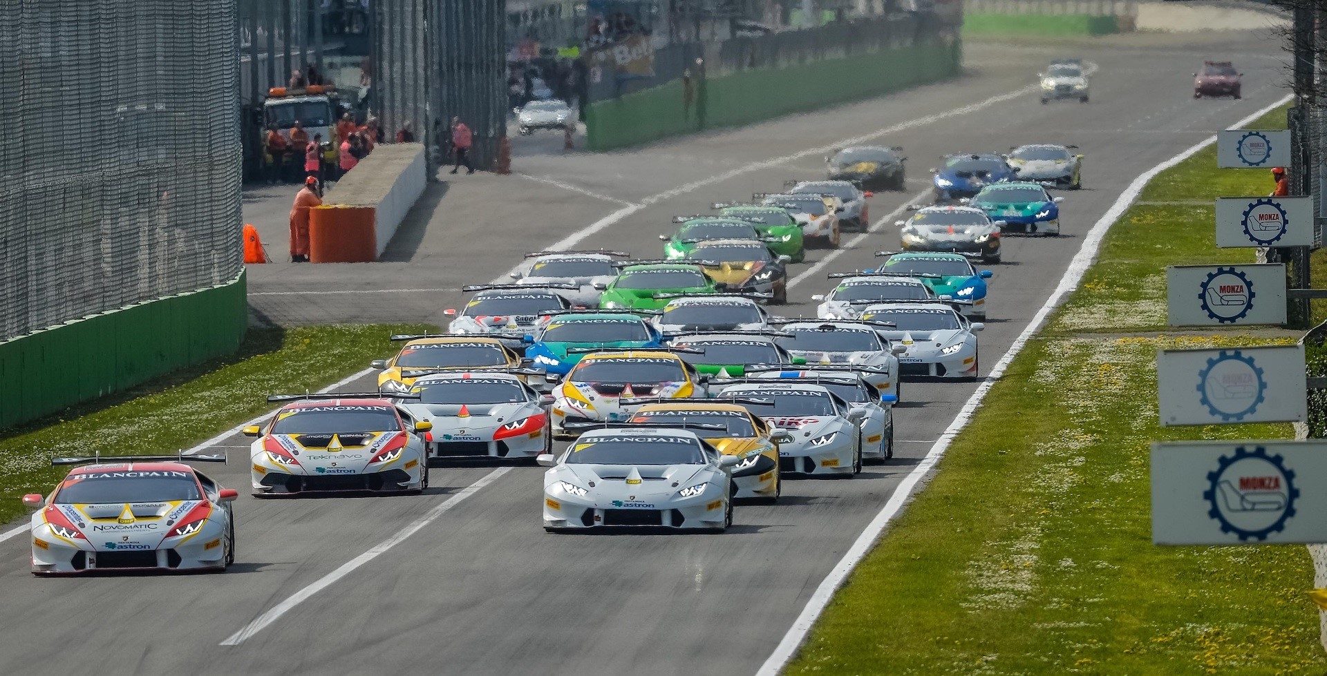 A packed grid of Lamborghini Huracán LP 620-2 Super Trofeo race cars in multi-colored liveries lined up on a circuit, viewed from an elevated front angle with spectators and officials in the background.