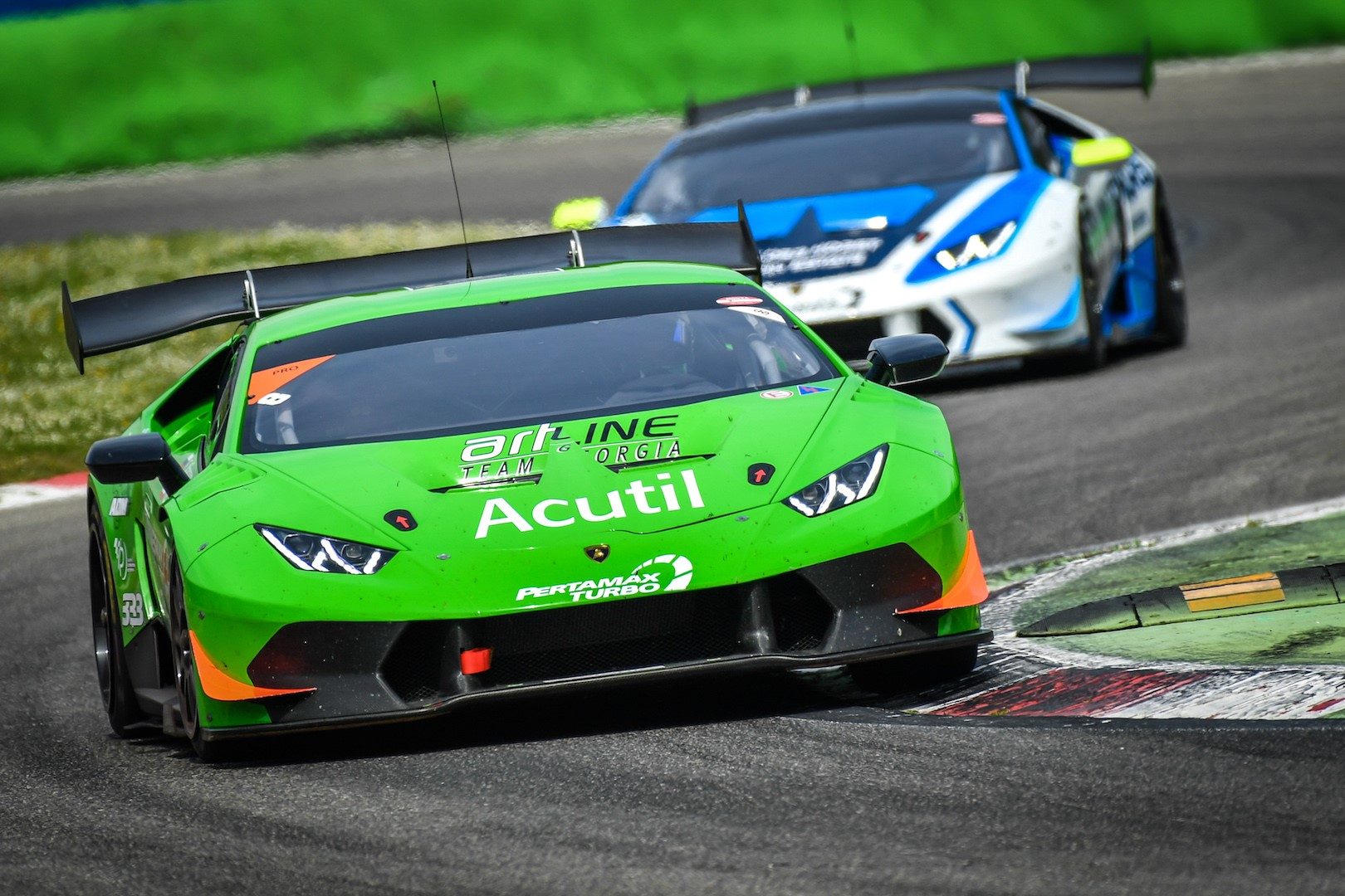 Green Lamborghini Huracán Super Trofeo race car leading a blue and white competitor on track during a Super Trofeo Europe race