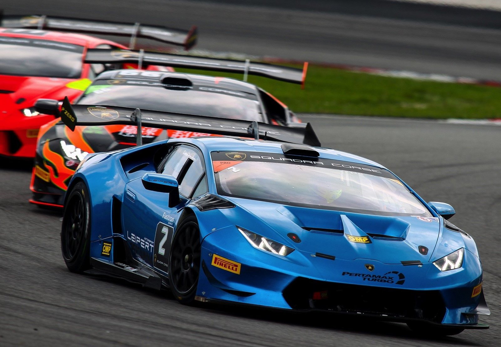 Lamborghini Huracán Super Trofeo race cars in close formation on a racing circuit, showing large rear wings and aggressive aerodynamic bodywork