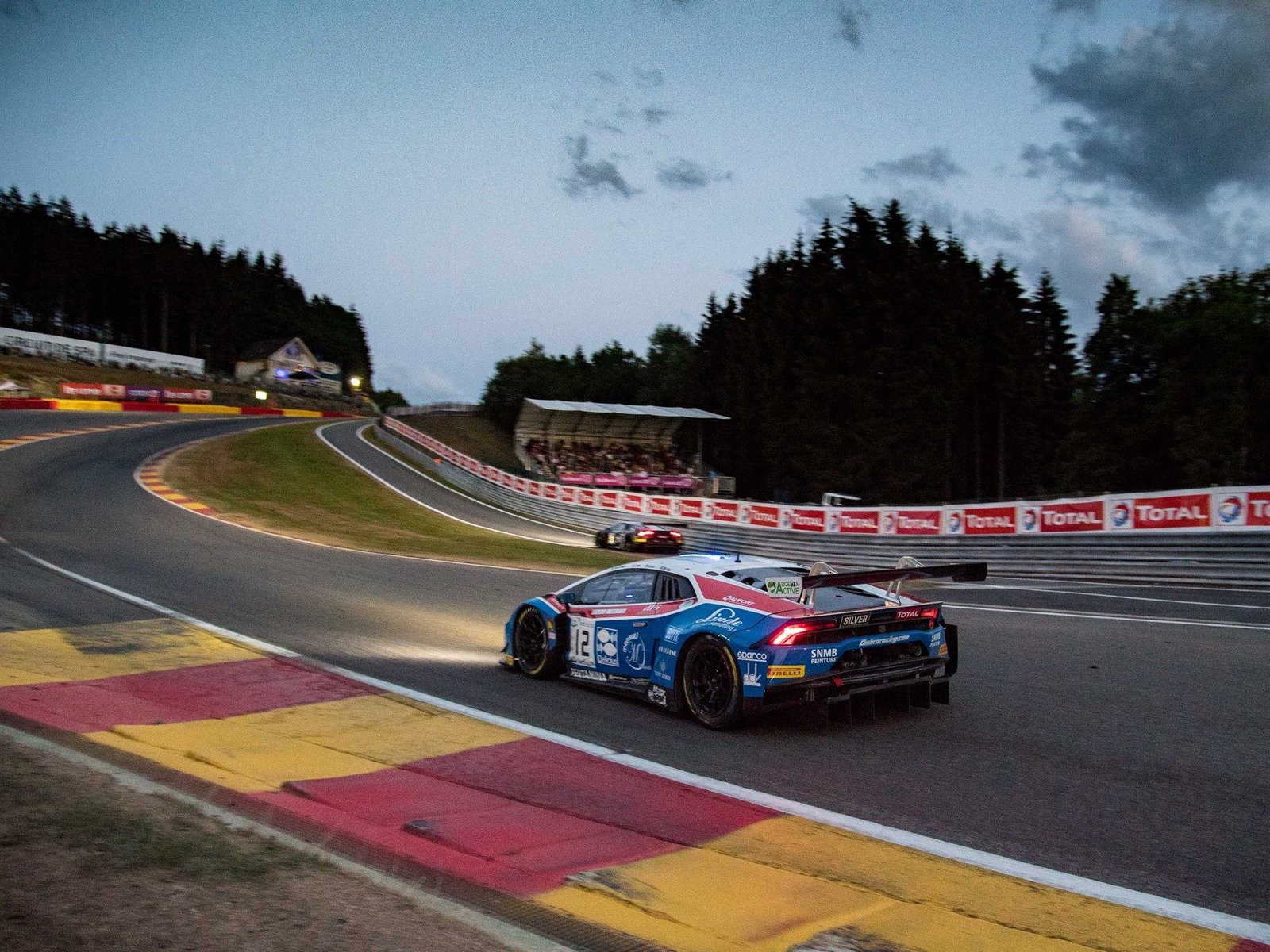Lamborghini Huracán GT3 Evo number 12 racing at twilight at Spa-Francorchamps with rear wing and headlights visible