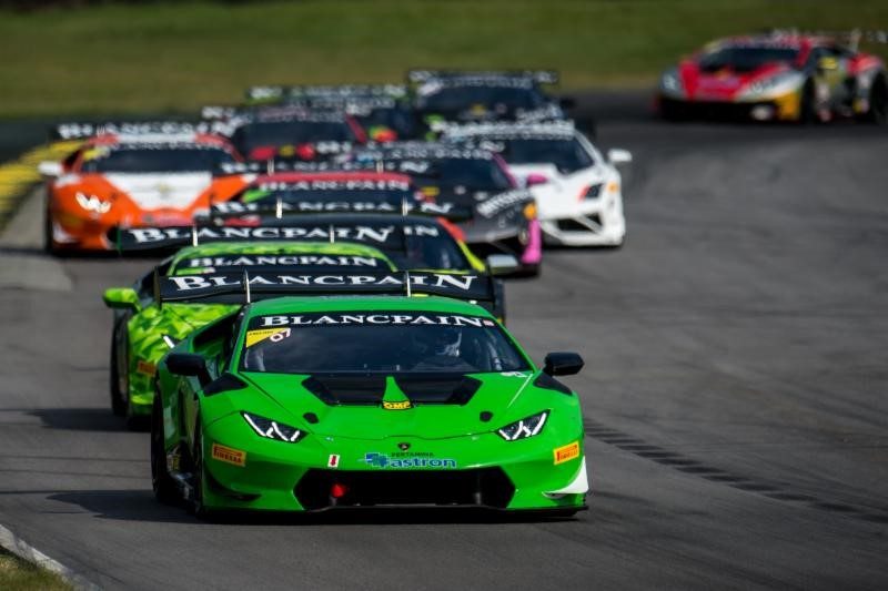 A pack of Lamborghini Huracán Super Trofeo race cars led by a green car speed down a racetrack during a Blancpain Super Trofeo North America event