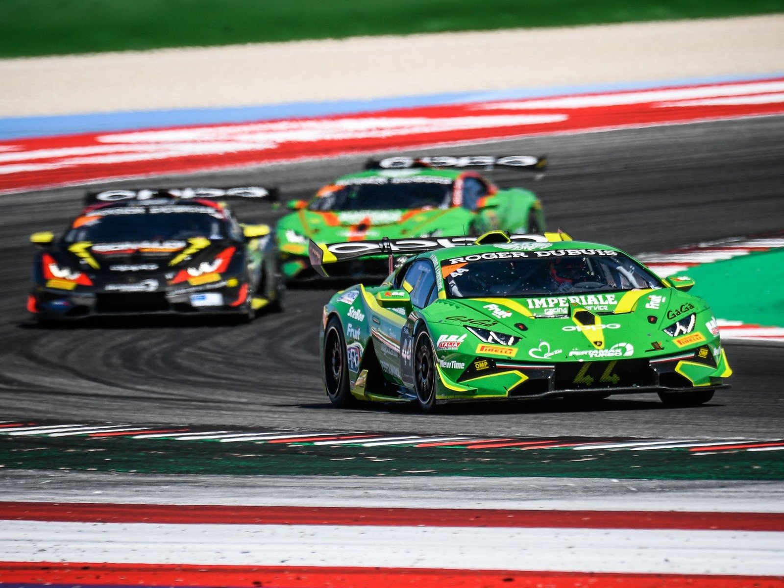 Three Lamborghini Huracán Super Trofeo EVO race cars battling for position on track, with a green car leading
