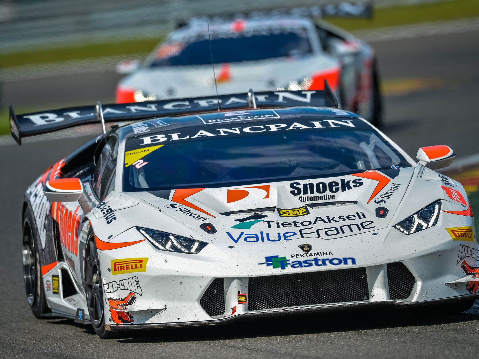 White Lamborghini Huracán Super Trofeo race car with orange accents racing on track with another car in the background