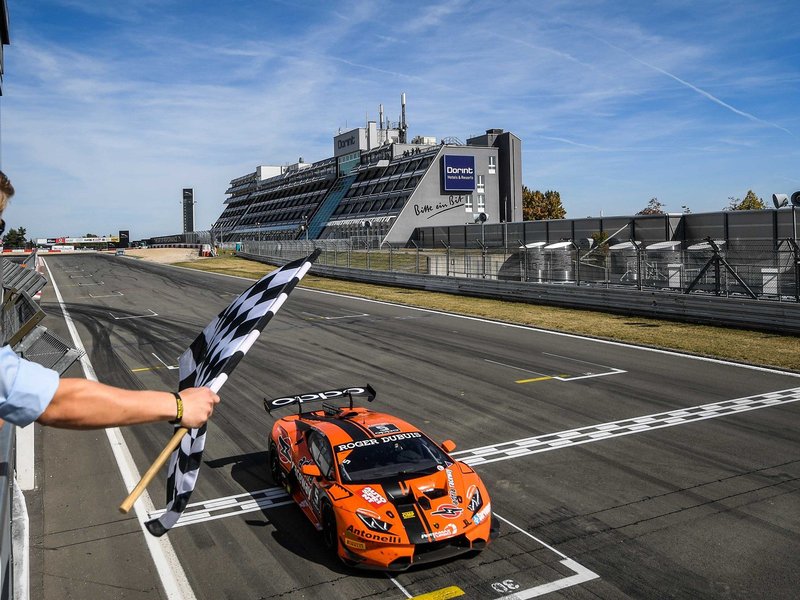 Orange Lamborghini Huracán Super Trofeo race car crosses the finish line at Nürburgring under the checkered flag