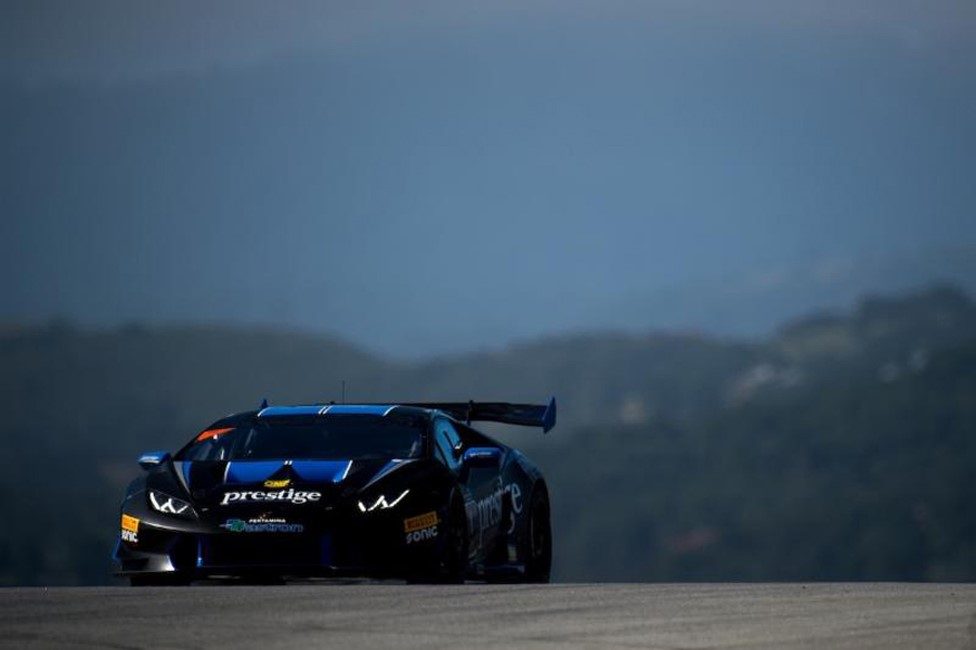 Black and blue Lamborghini Huracán Super Trofeo race car at speed on track with mountainous backdrop