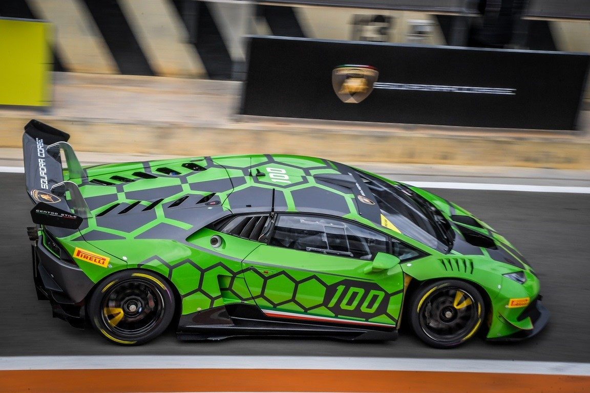 A green and black Lamborghini Huracán Super Trofeo race car at speed on a racetrack, featuring aggressive aerodynamics and a large rear wing