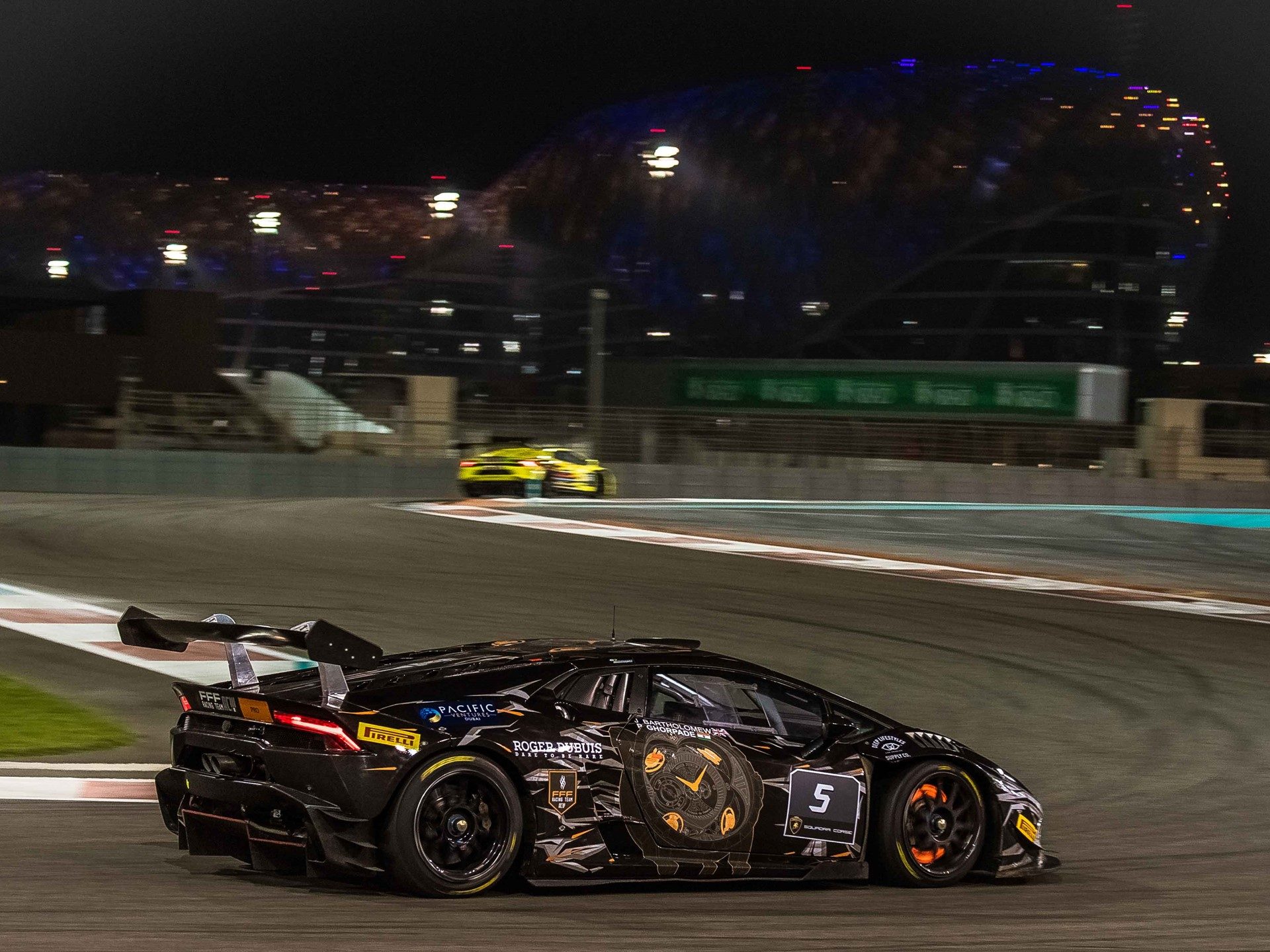 Black Lamborghini Huracán Super Trofeo race car with orange accents racing under floodlights at Yas Marina Circuit