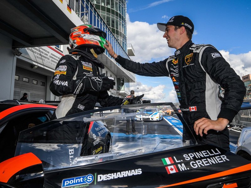 Two Lamborghini Super Trofeo drivers interact beside a black and orange Huracán Super Trofeo Evo on the Nürburgring grid