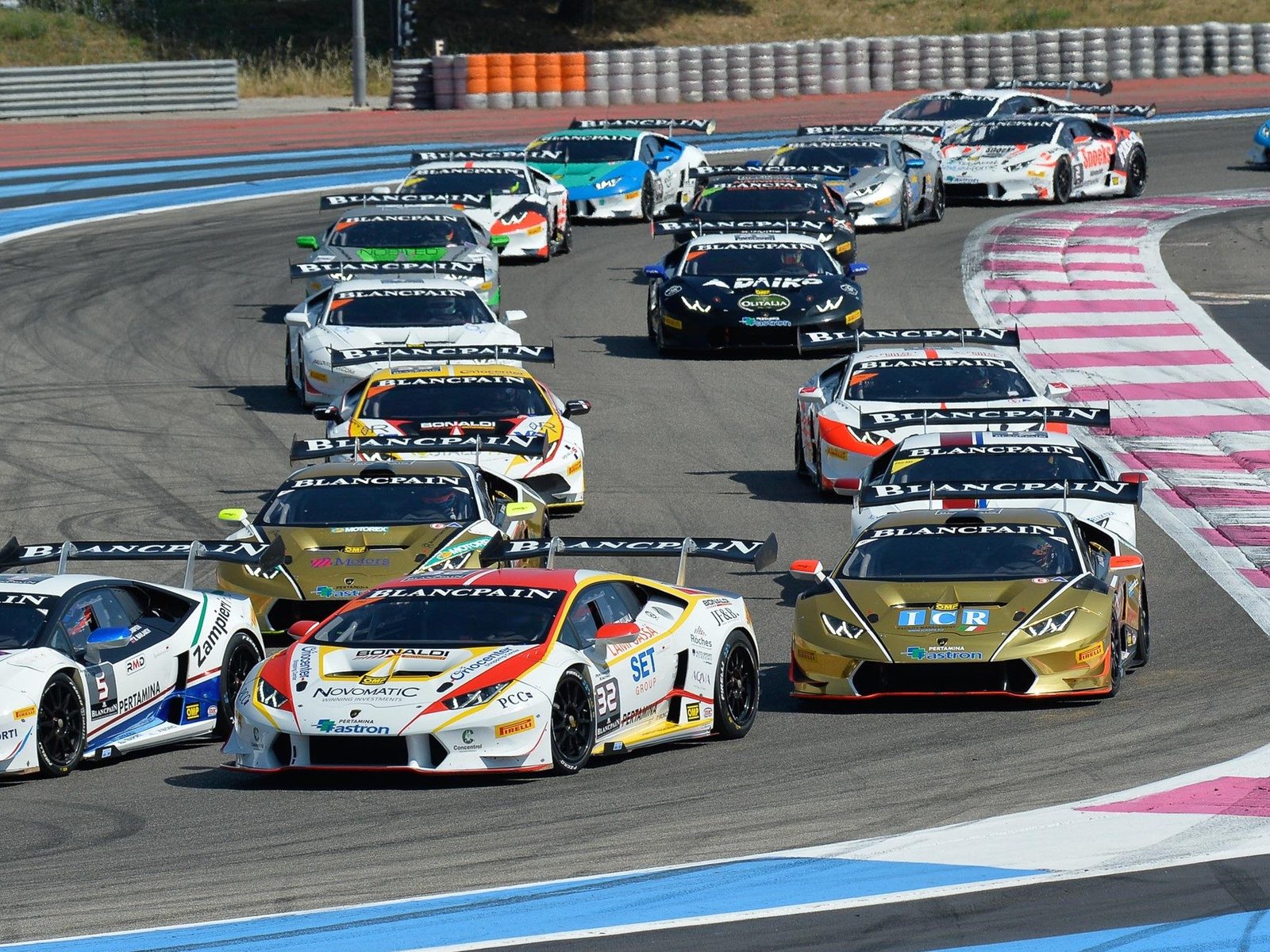 A fleet of Lamborghini Huracán Super Trofeo race cars in various liveries navigating a turn on a race circuit during the Blancpain Super Trofeo series