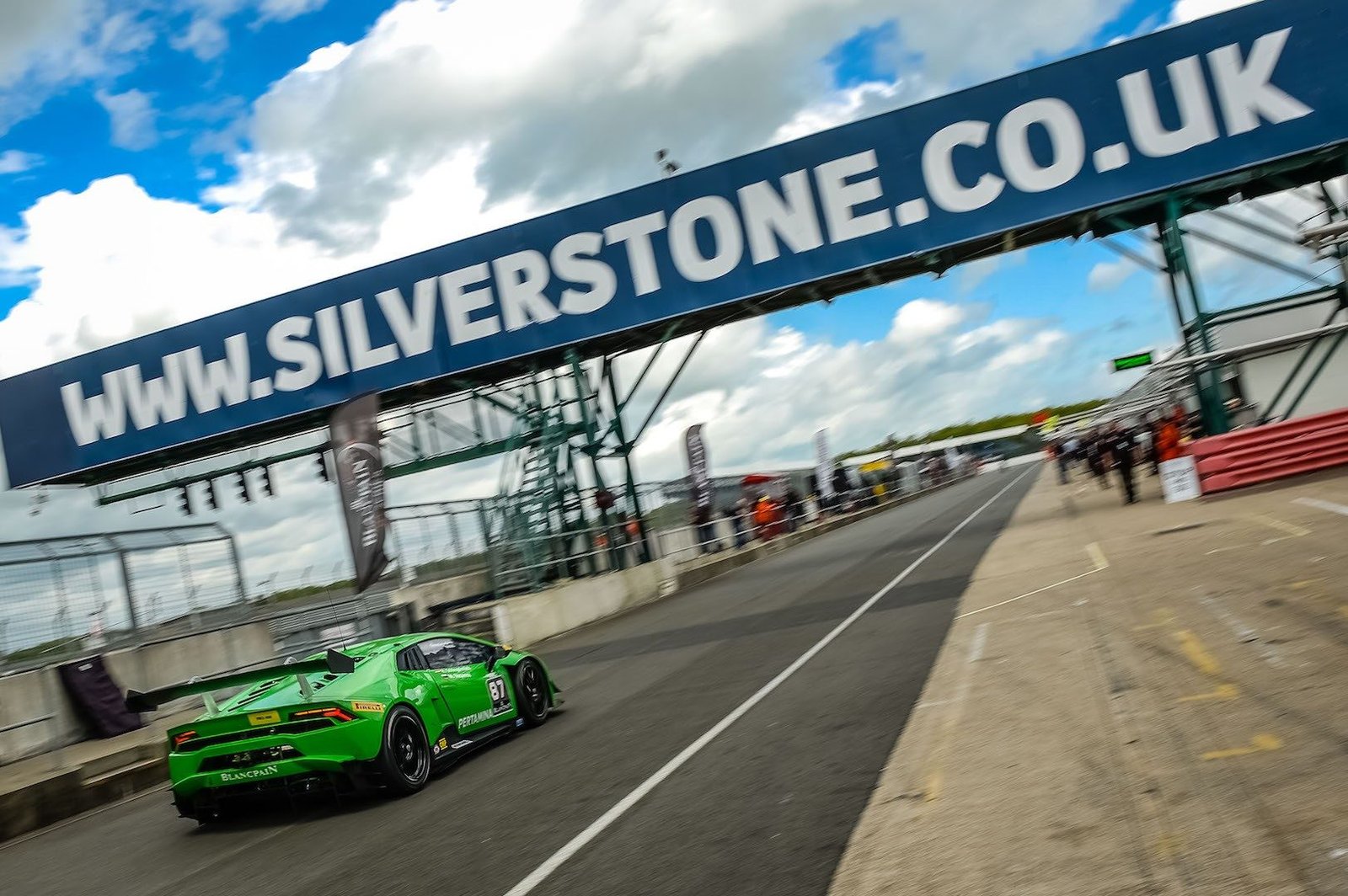 Green Lamborghini Huracán race car at speed on the Silverstone circuit with motion blur and spectators in the background