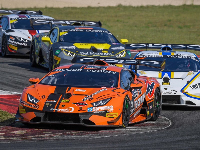 An orange Lamborghini Huracán Super Trofeo Evo leads a pack of identical race cars through a corner during a Super Trofeo Europe race