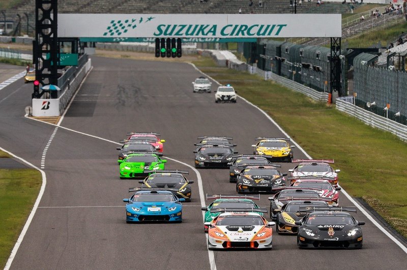Pack of multi-colored Lamborghini Huracán Super Trofeo race cars launching from the grid at Suzuka Circuit under green lights