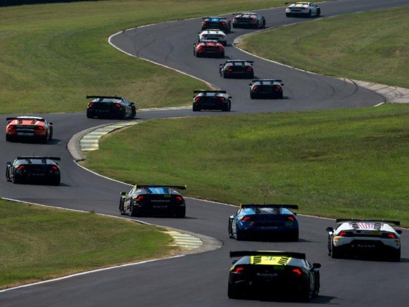 A pack of Lamborghini Huracán Super Trofeo race cars in various liveries navigating a winding circuit during competition