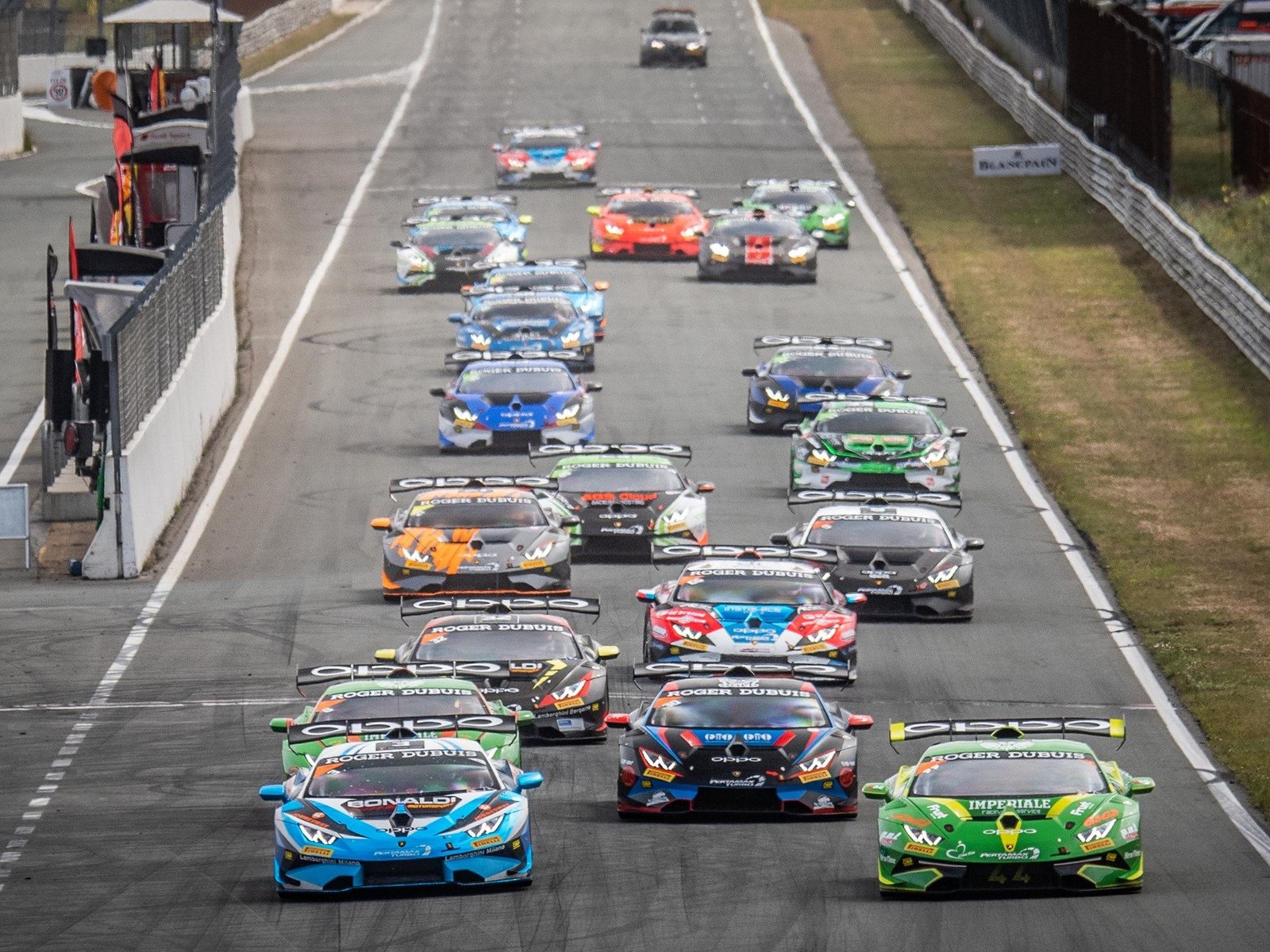 Full grid of Lamborghini Huracán Super Trofeo Evo race cars lined up on track in vibrant racing liveries with large rear wings and aggressive aerodynamic kits