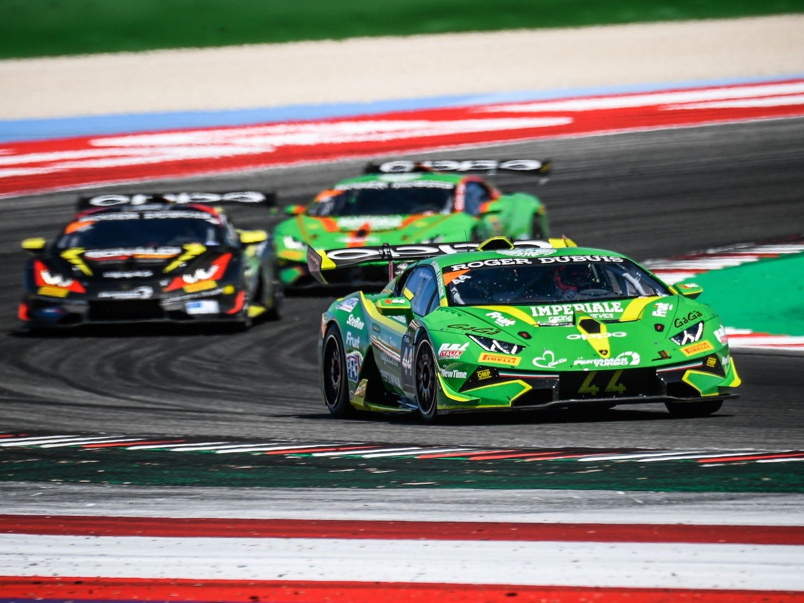 Three Lamborghini Huracán Super Trofeo EVO race cars battling for position on track, showing aggressive aero packages and large rear wings