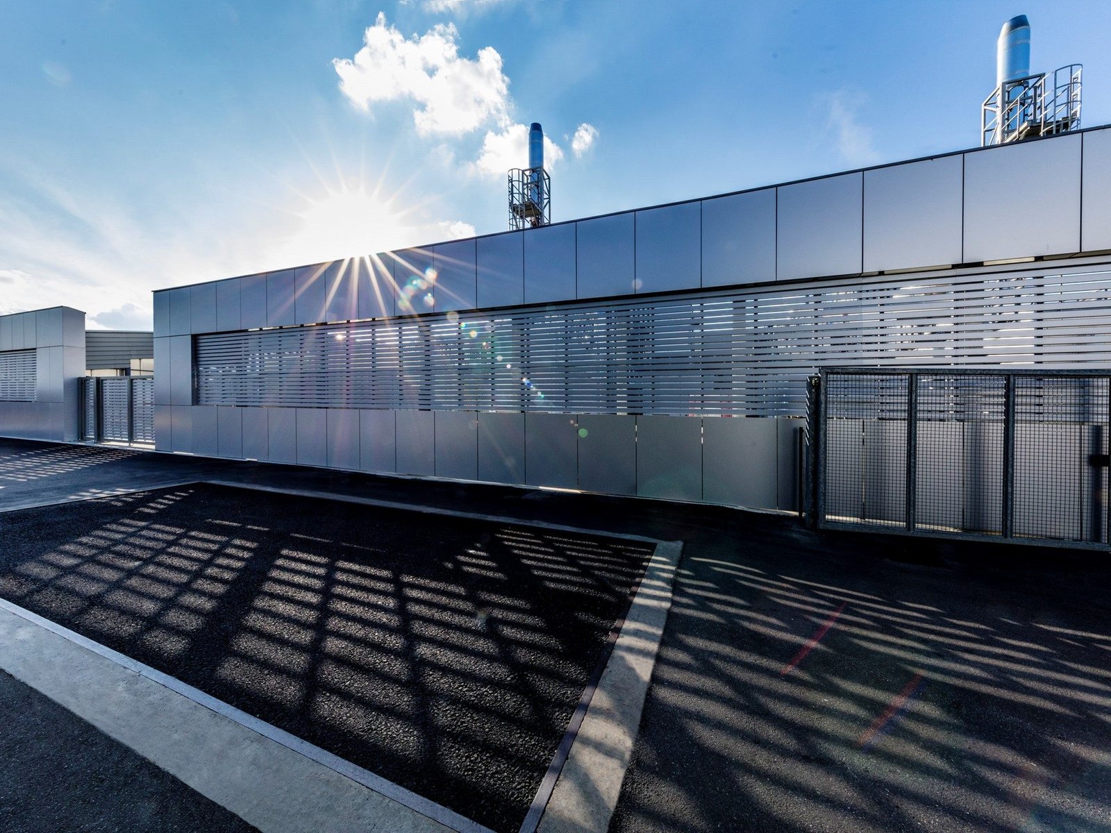 Modern industrial building at Lamborghini's Sant'Agata Bolognese factory with silver metallic panels, horizontal louvers, and rooftop chimney structure