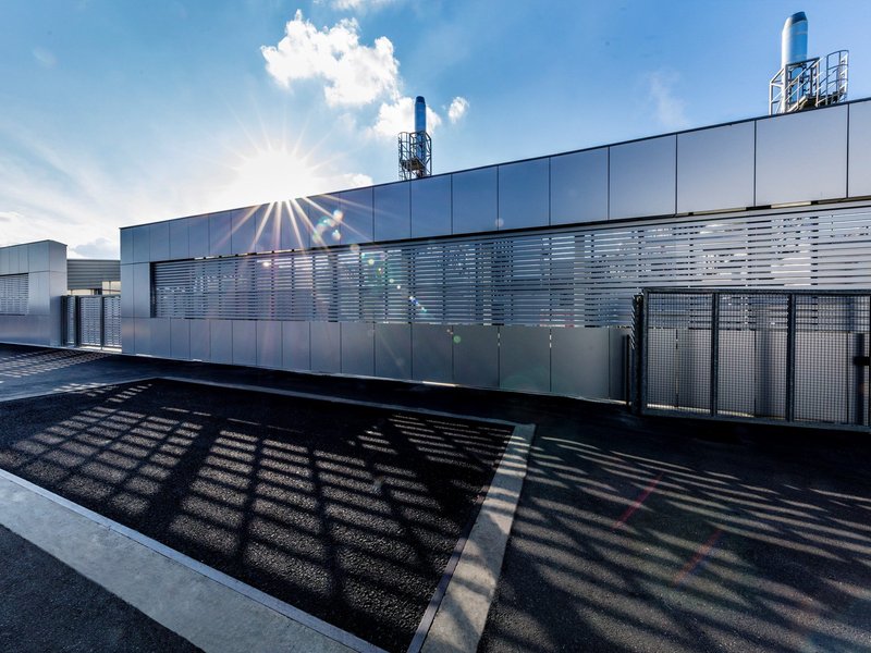 Modern industrial building at Lamborghini's Sant'Agata Bolognese factory with silver metallic panels, horizontal louvers, and rooftop chimney structure