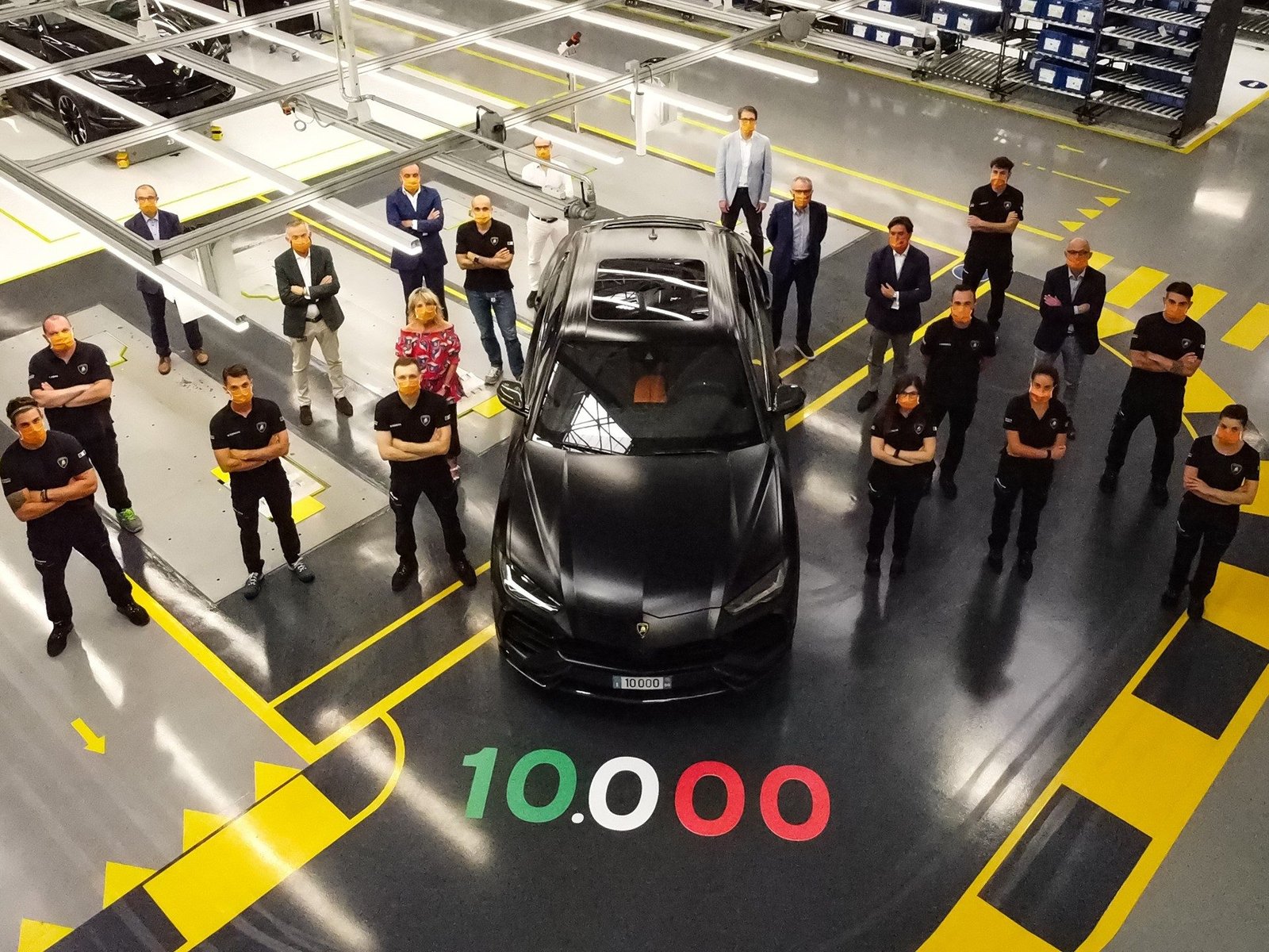 Overhead view of the 10,000th Lamborghini Urus in matte black surrounded by Lamborghini employees in the Sant'Agata Bolognese factory, with '10.000' painted on the floor in Italian flag colors