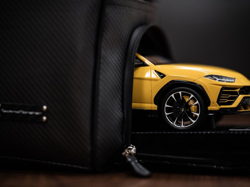 Yellow Lamborghini Urus scale model emerging from a black carbon fiber-textured bag