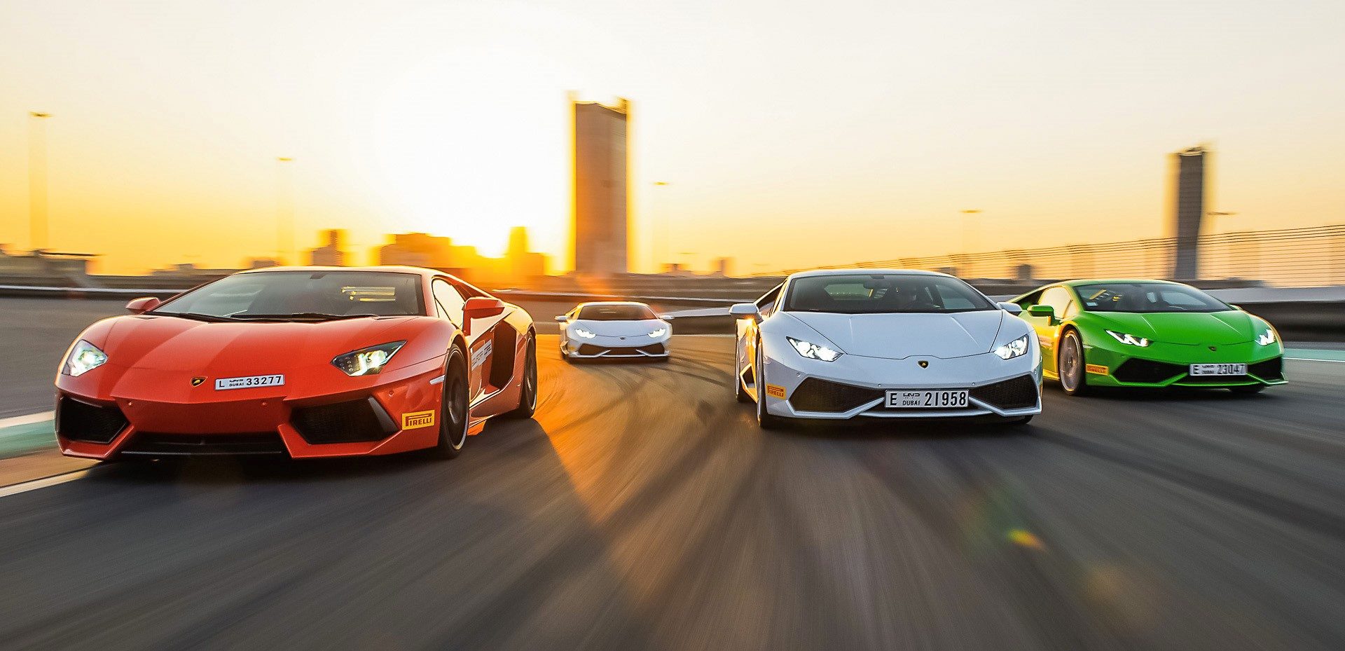 Multiple Lamborghini supercars racing on a circuit at sunset, showcasing the Aventador and Huracán models in vibrant colors