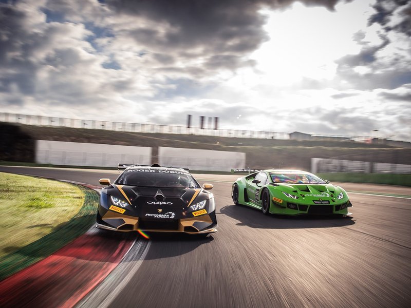 Two Lamborghini Huracán GT3 EVO race cars in action on track, featuring aggressive aerodynamic kits, large rear wings, and distinct racing liveries.