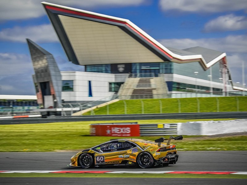 Gold Lamborghini Huracán Super Trofeo race car at speed on the Silverstone circuit under blue skies