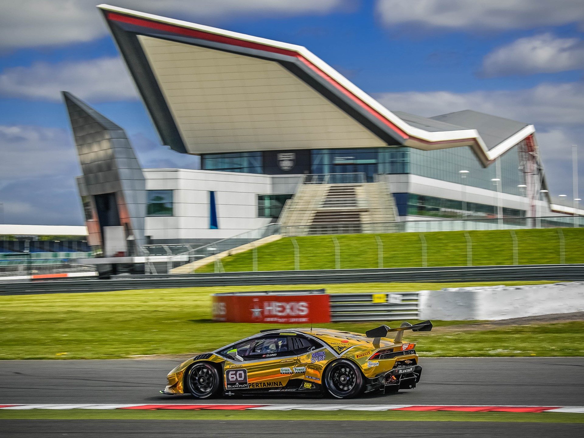 Gold Lamborghini Huracán Super Trofeo race car at speed on the Silverstone circuit under blue skies