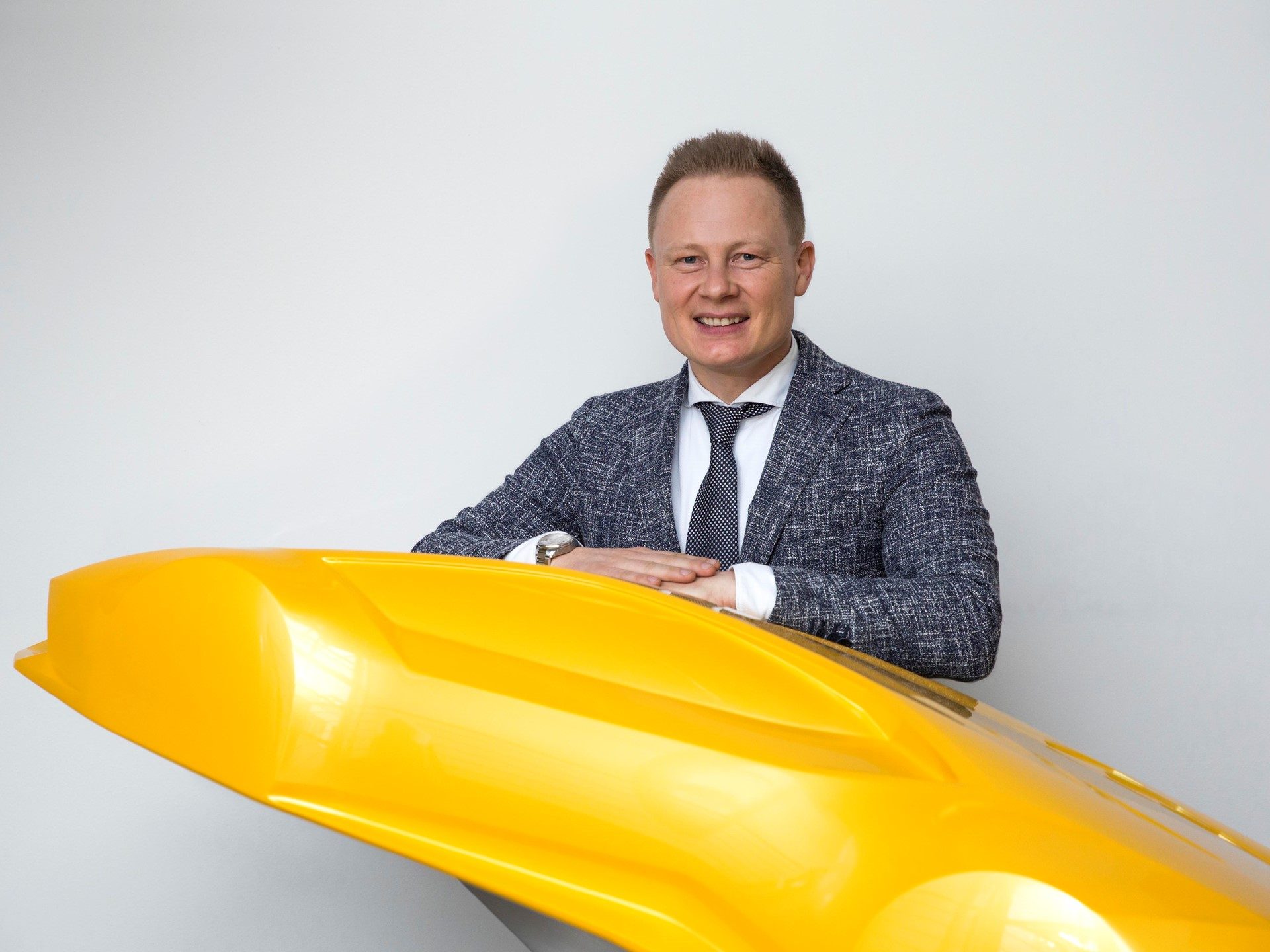 Mitja Borkert, Lamborghini Design Director, leaning on a bright yellow sculptural automotive form