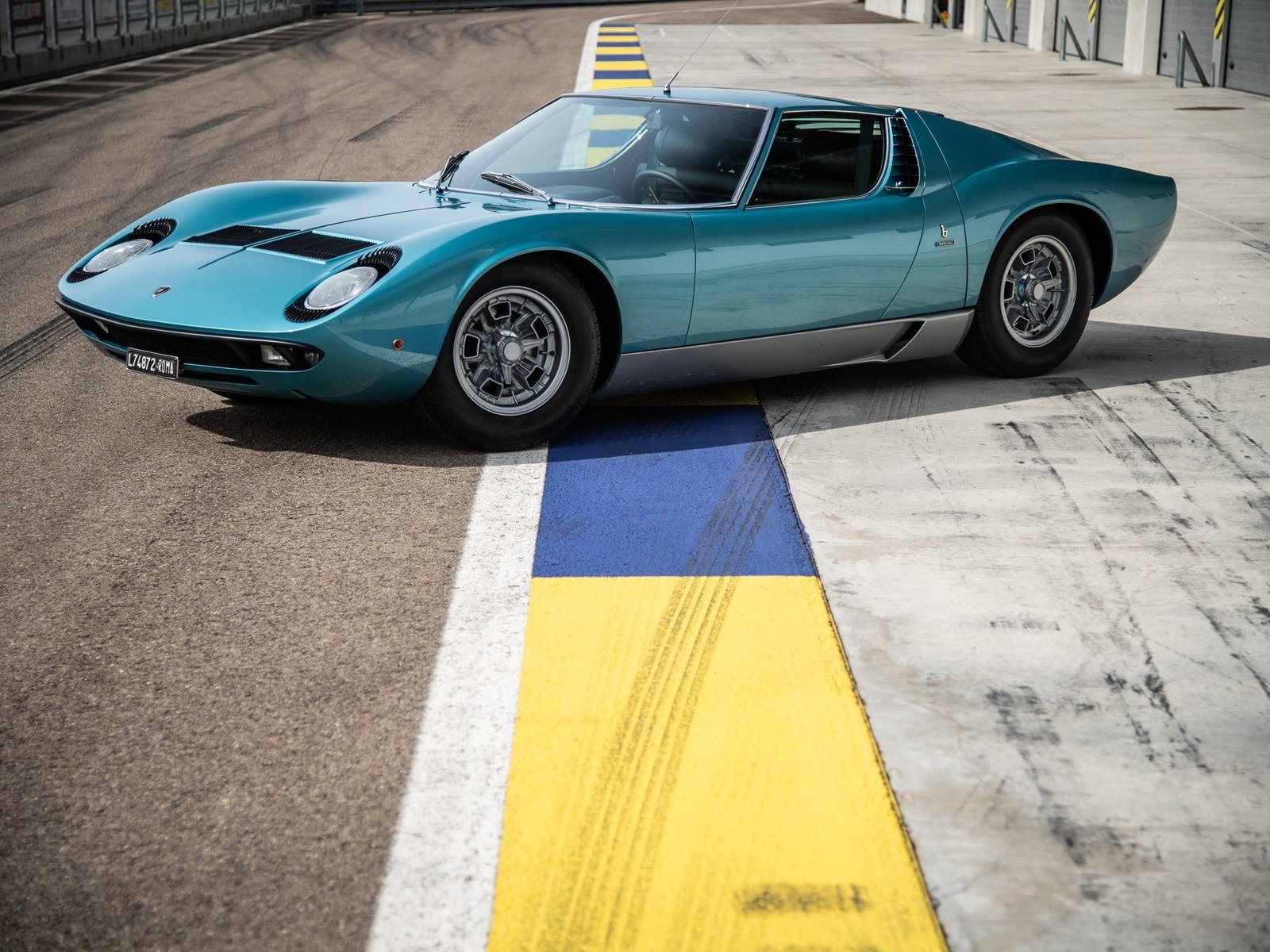 Lamborghini Miura P400 in Azzurro Mexico blue parked on a racetrack, showcasing its iconic mid-engine profile and pop-up headlights