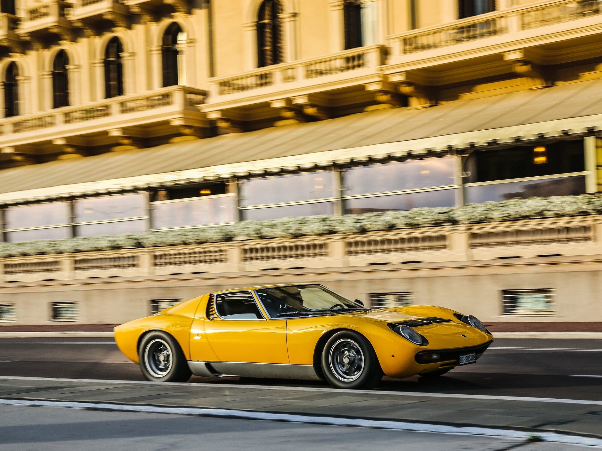 Classic yellow Lamborghini Miura P400 in motion past a grand European building