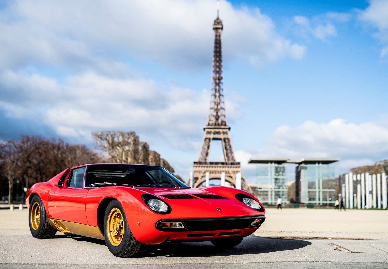 Restored Lamborghini Miura SV in Rosso Corsa with gold wheels posed in front of the Eiffel Tower in Paris