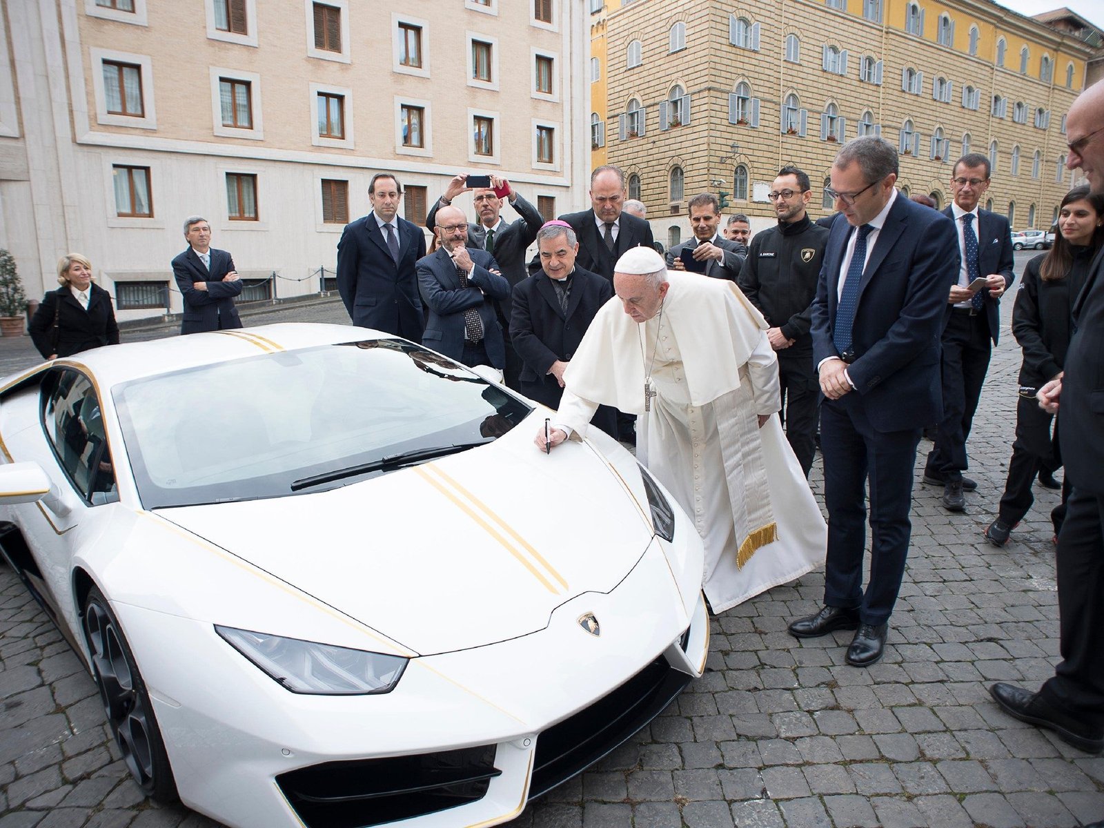 Pope Francis signing the hood of the white and gold Lamborghini Huracán RWD at the Vatican, surrounded by Lamborghini executives