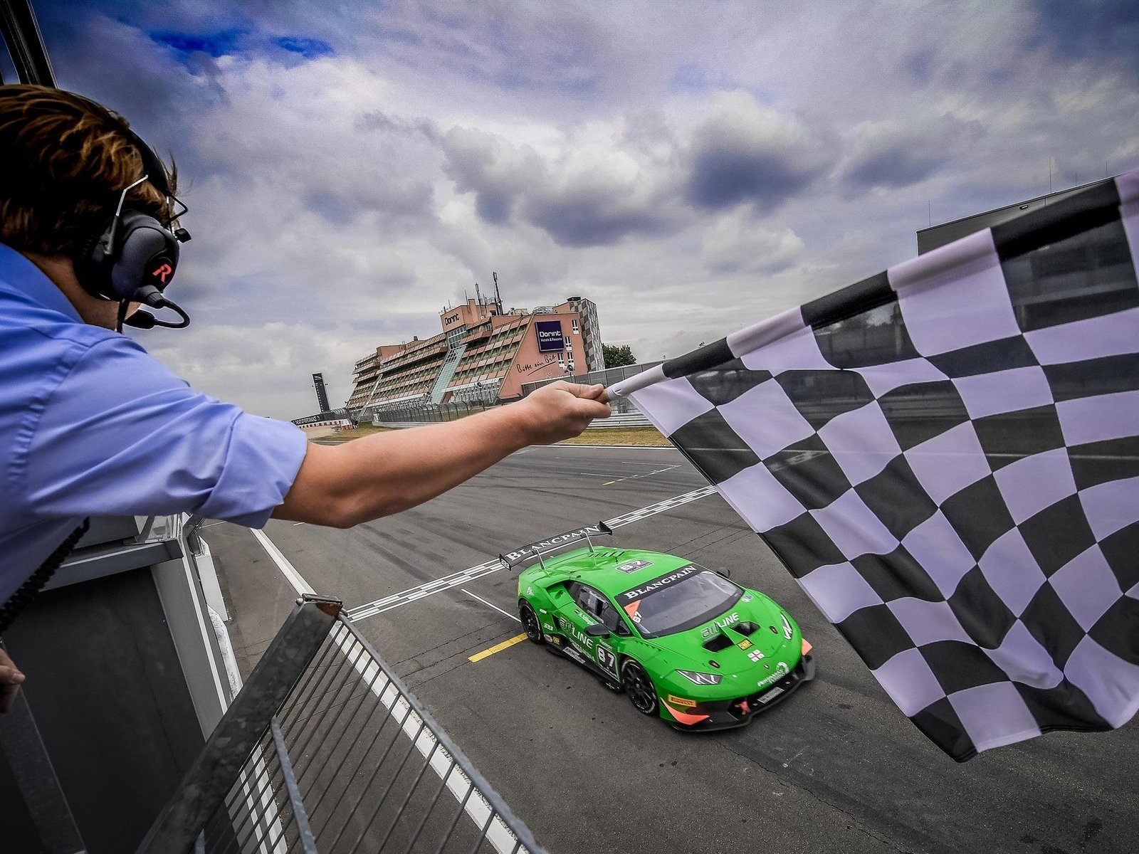 A green Lamborghini Huracán race car crosses the finish line under a checkered flag at the Nürburgring