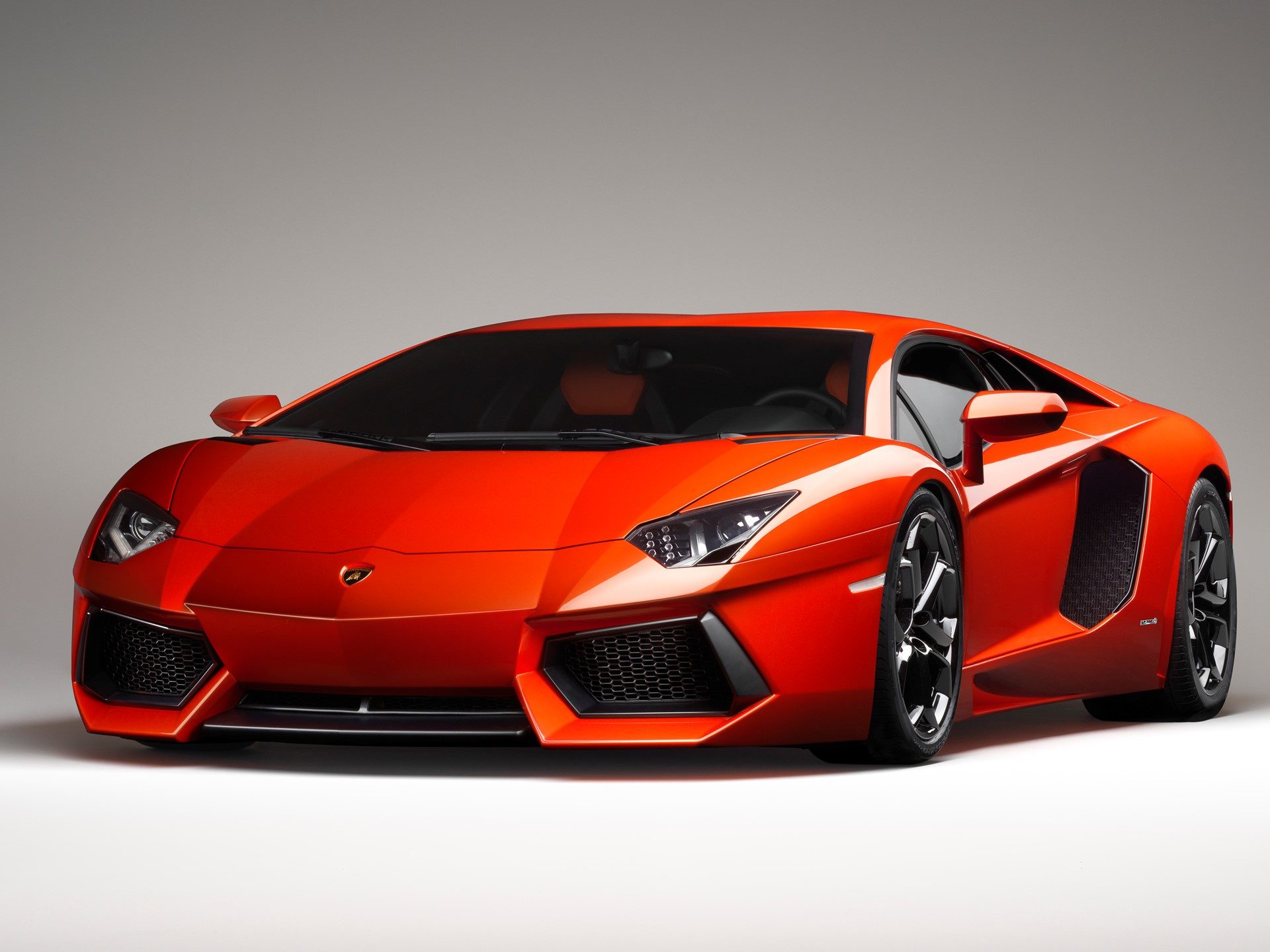 Orange Lamborghini Aventador LP700-4 in studio lighting, highlighting the Y-shaped LED headlights and carbon fiber monocoque body