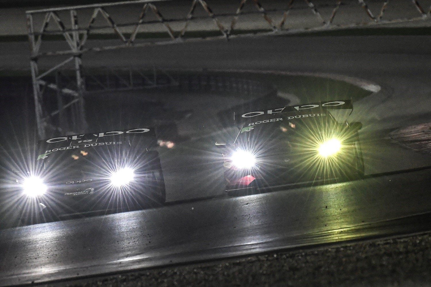Two Lamborghini Huracán Super Trofeo race cars competing side-by-side under floodlights at Sepang with LED headlights blazing