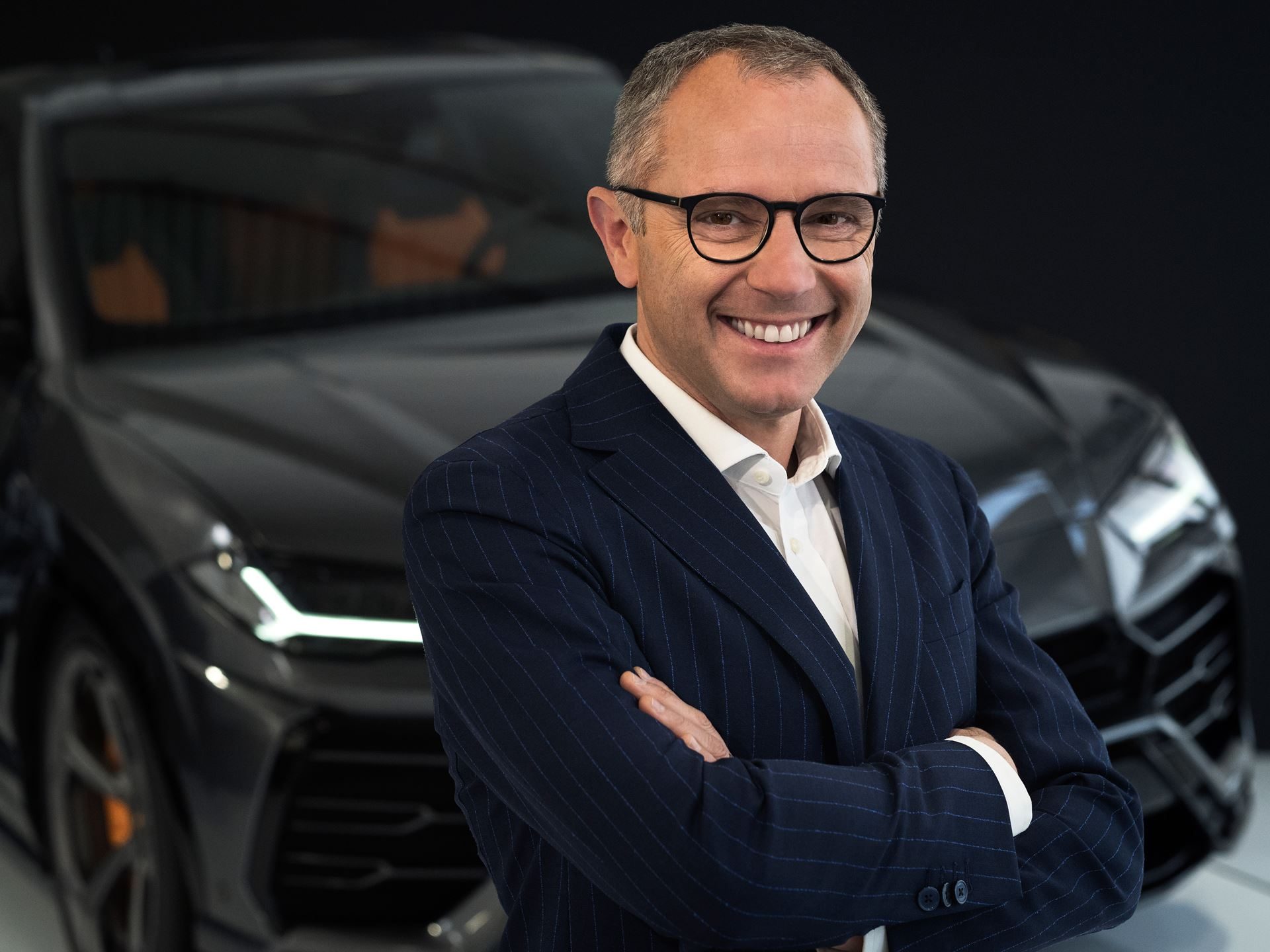 Stefano domenicali, former chairman and ceo of automobili lamborghini, standing with arms crossed in front of a lamborghini urus