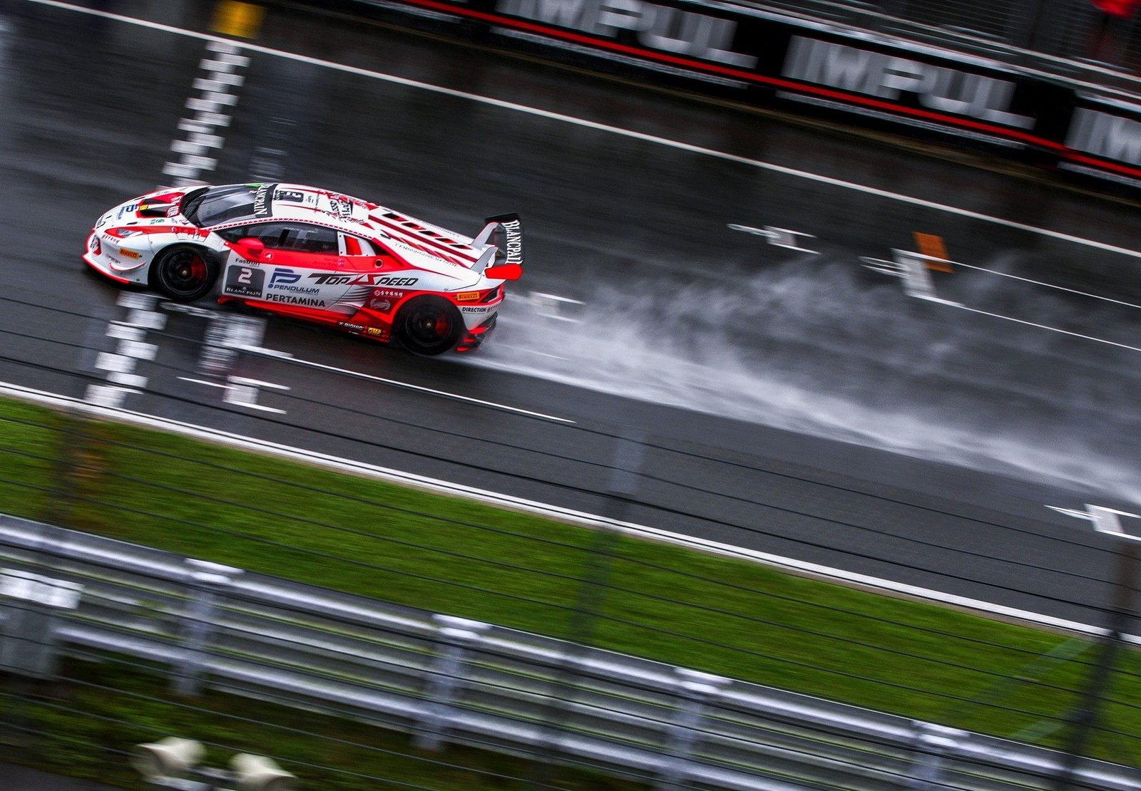 Lamborghini Huracán Super Trofeo race car speeds through heavy rain at Fuji Speedway, throwing up a wall of spray from its rear tires